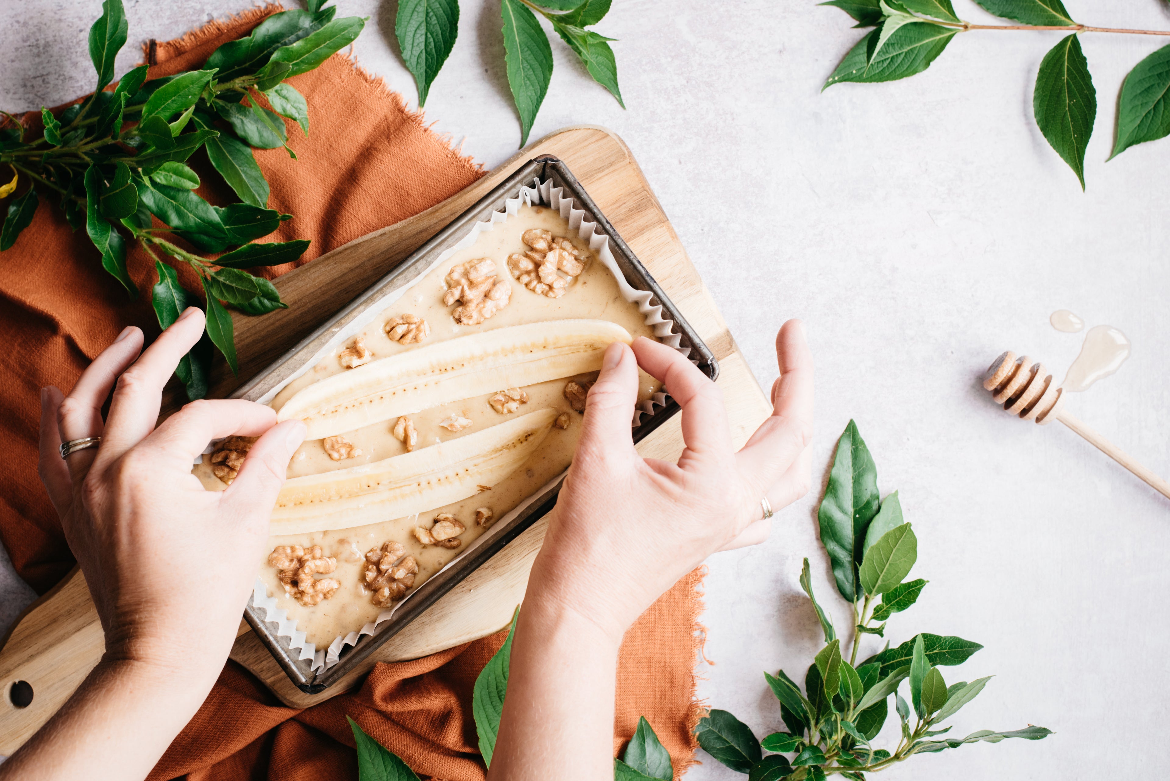 Hands placing sliced banana on top of an uncooked healthy banana bread loaf