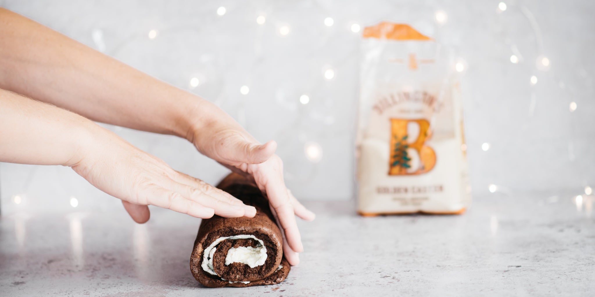 Yule log being rolled up with hands in shot and sugar pack in background