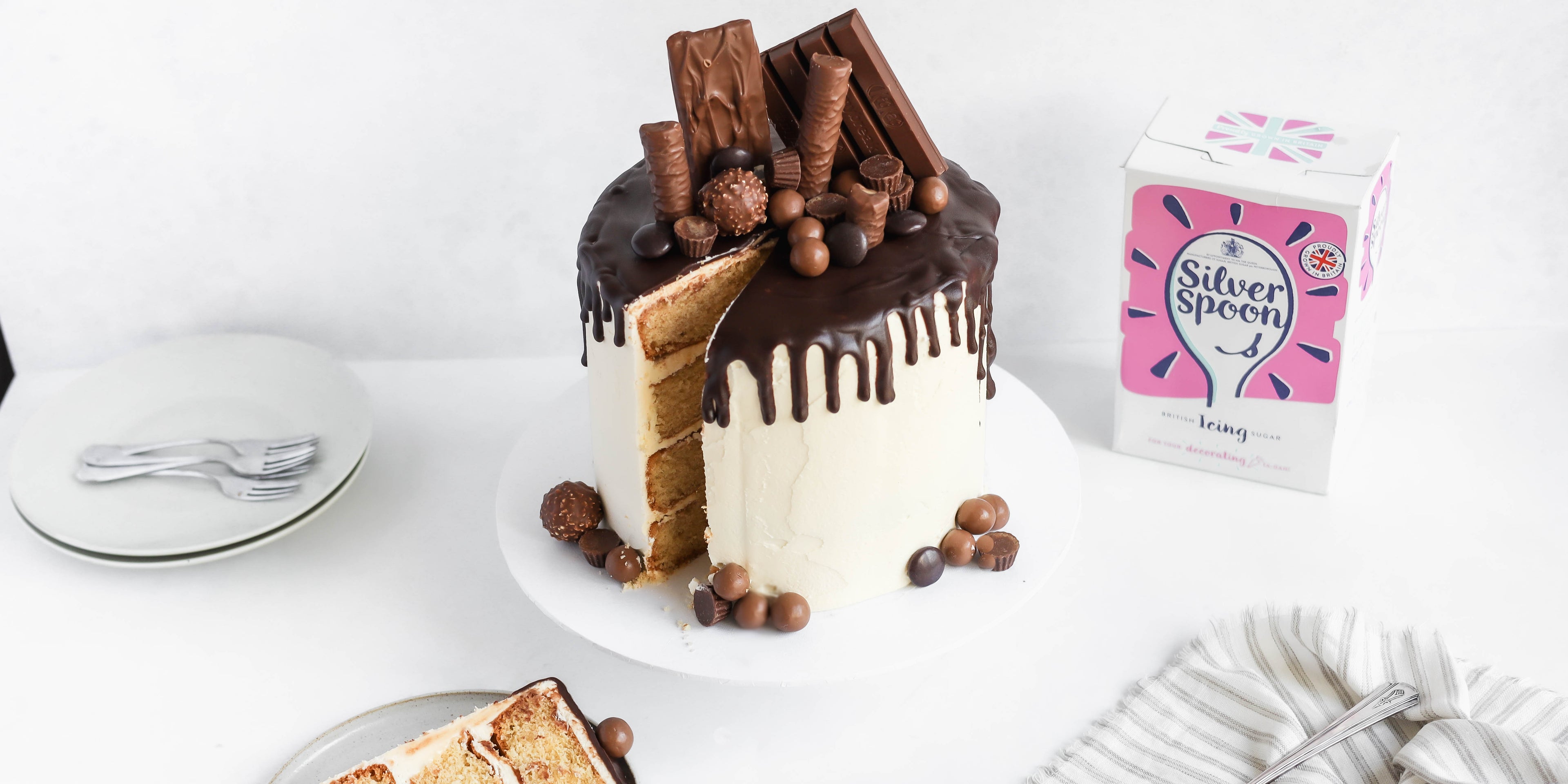 Ultimate Birthday Drip Cake with a slice cut out of it, next to a box of Silver Spoon icing sugar