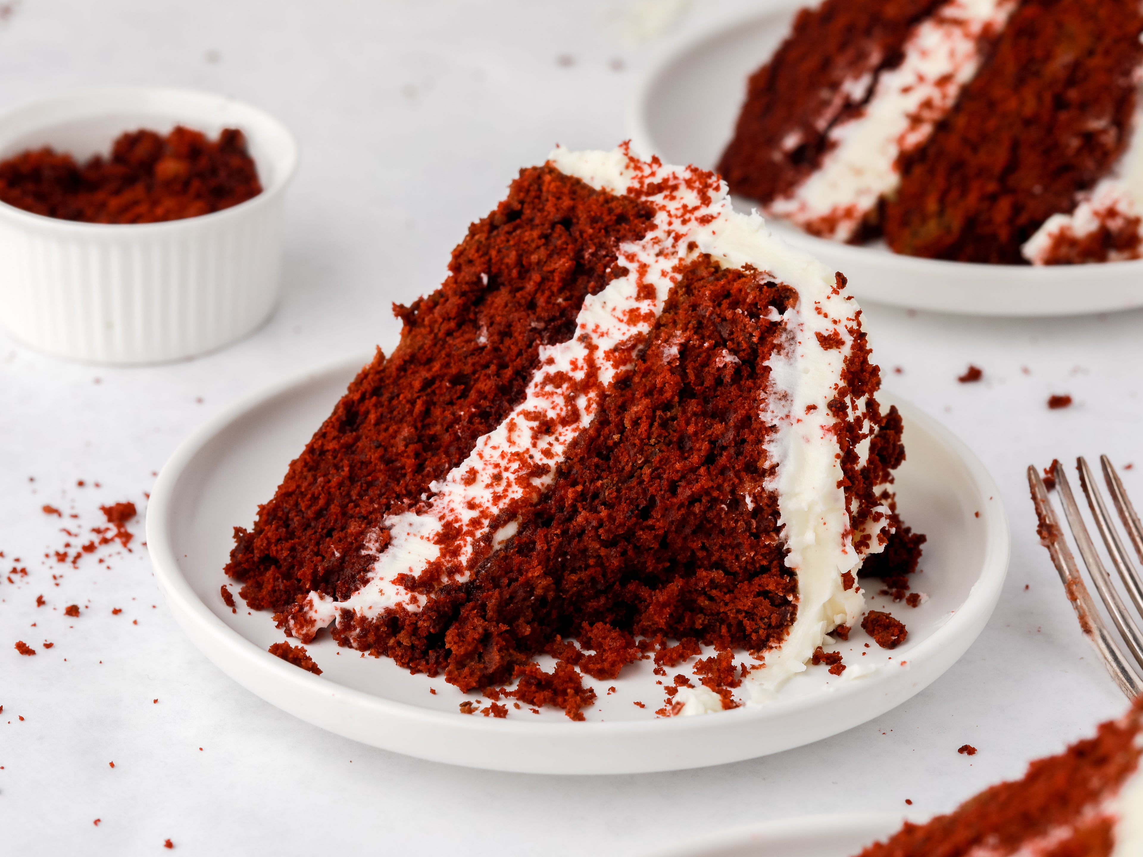 Close up of a slice of red velvet cake on a plate with a bite taken out of it