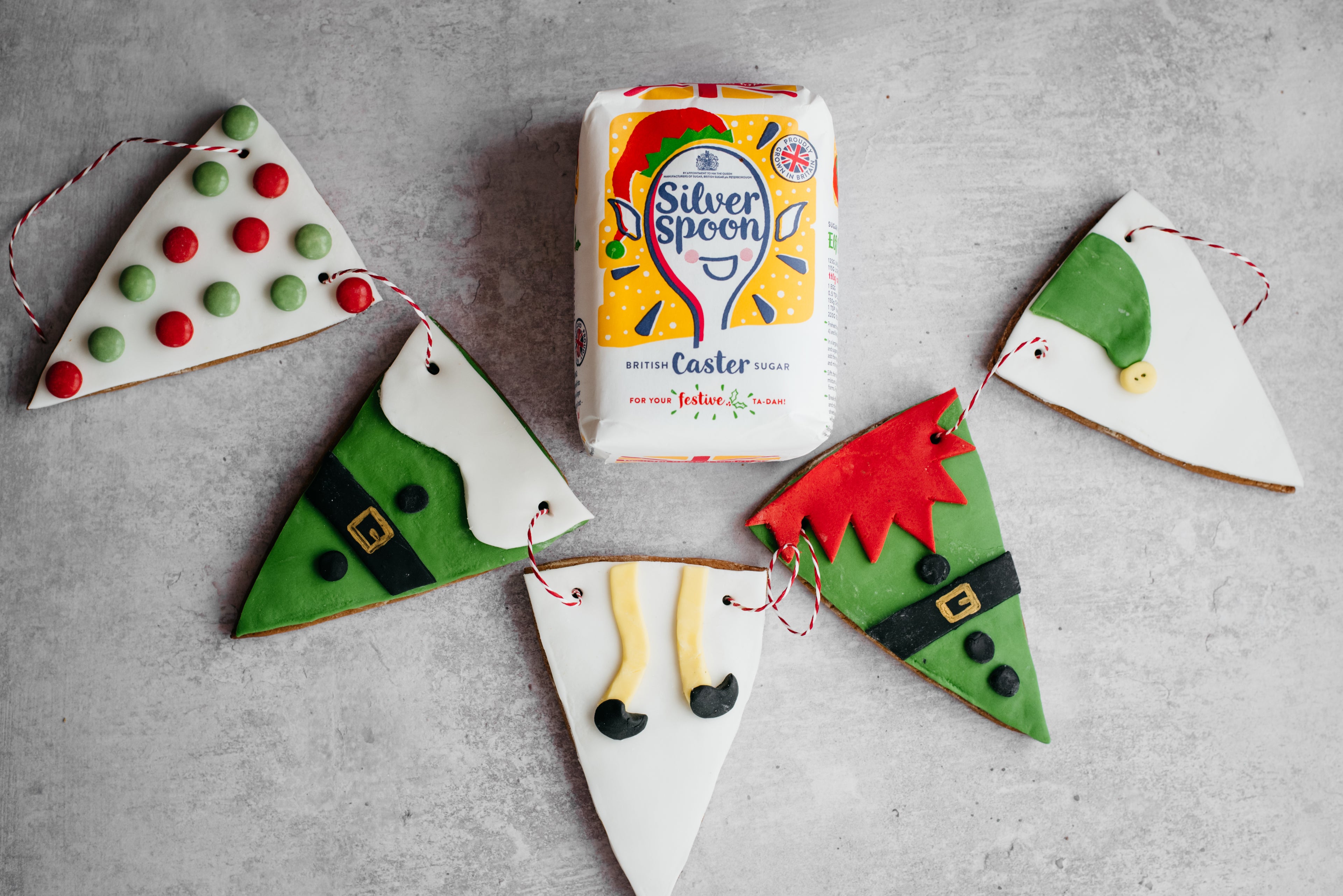 HoHoHo Elf Bunting close up, decorated with elf designs next to a bag of Christmas edition Silver Spoon caster sugar packaging