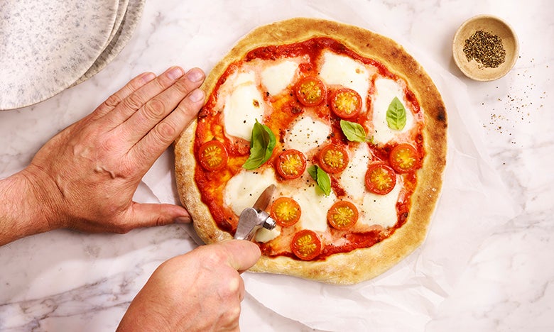 Cutting into a homemade margherita pizza using a pizza cutter