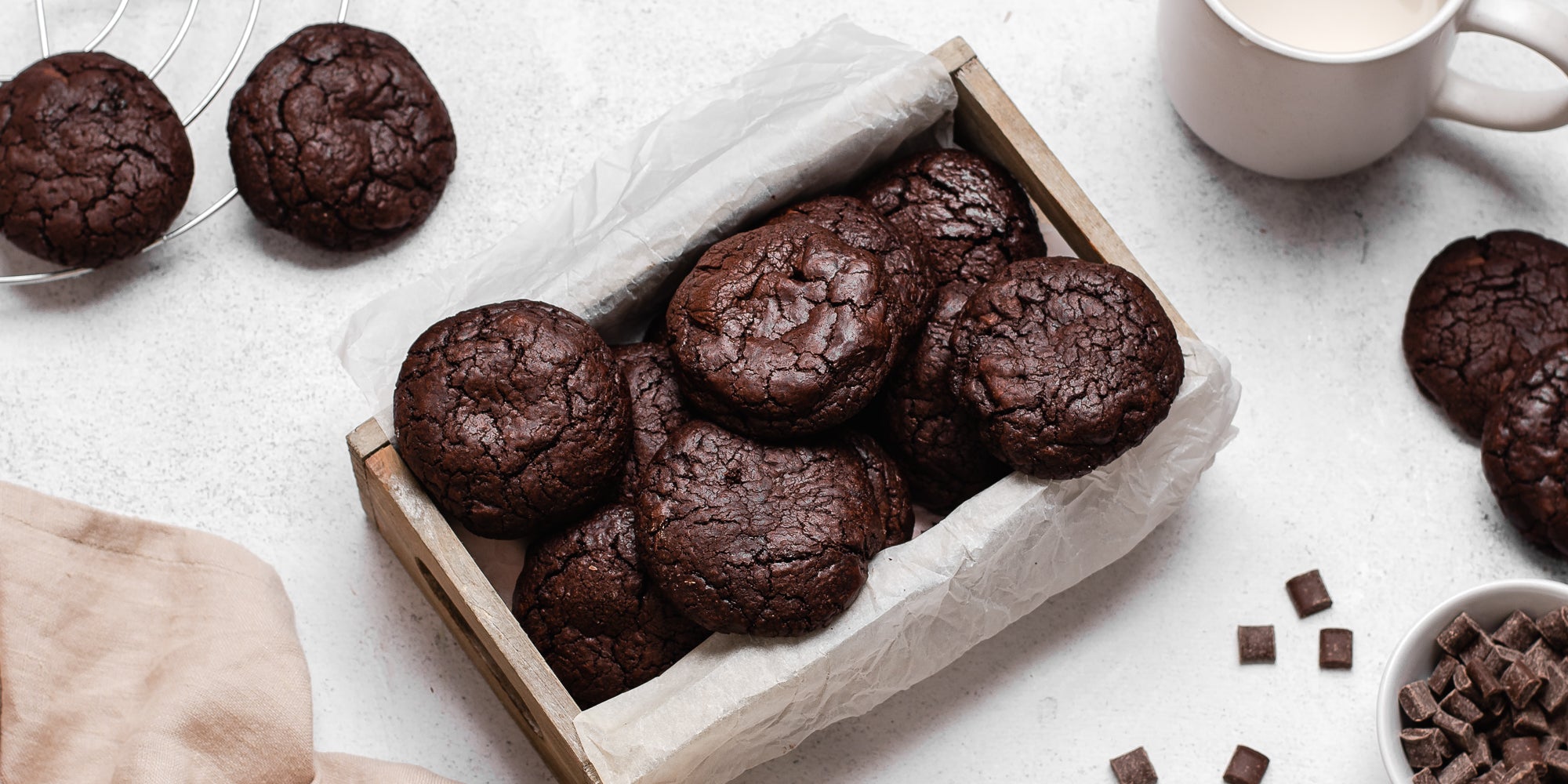 A fresh batch of Chocolate Brownie Cookies in a wooden box lined with baking parchment next to a glass of milk