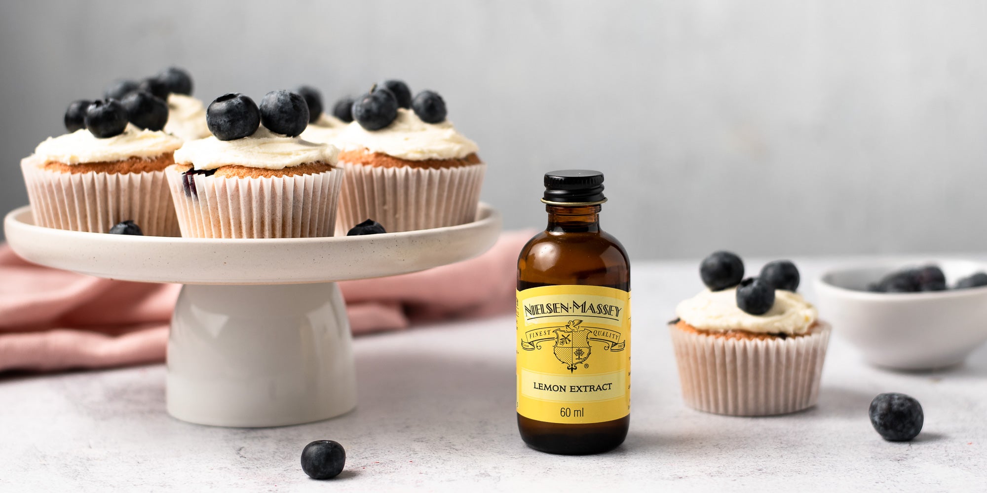 Cupcakes topped with icing and blueberries next to lemon extract