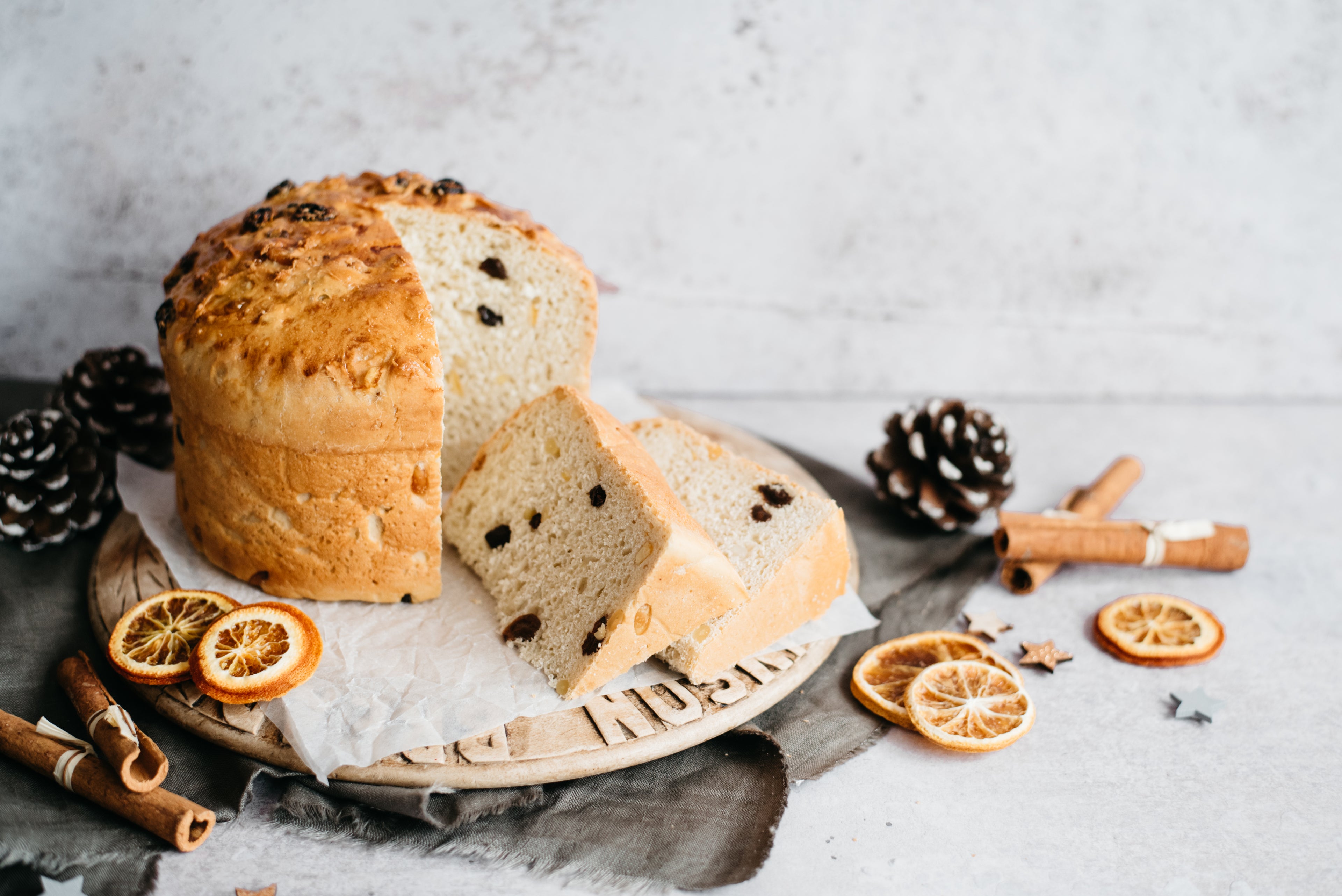 Panettone served on a wooden serving board, with a slice cut out showing the fluffy, fruit filled insides.