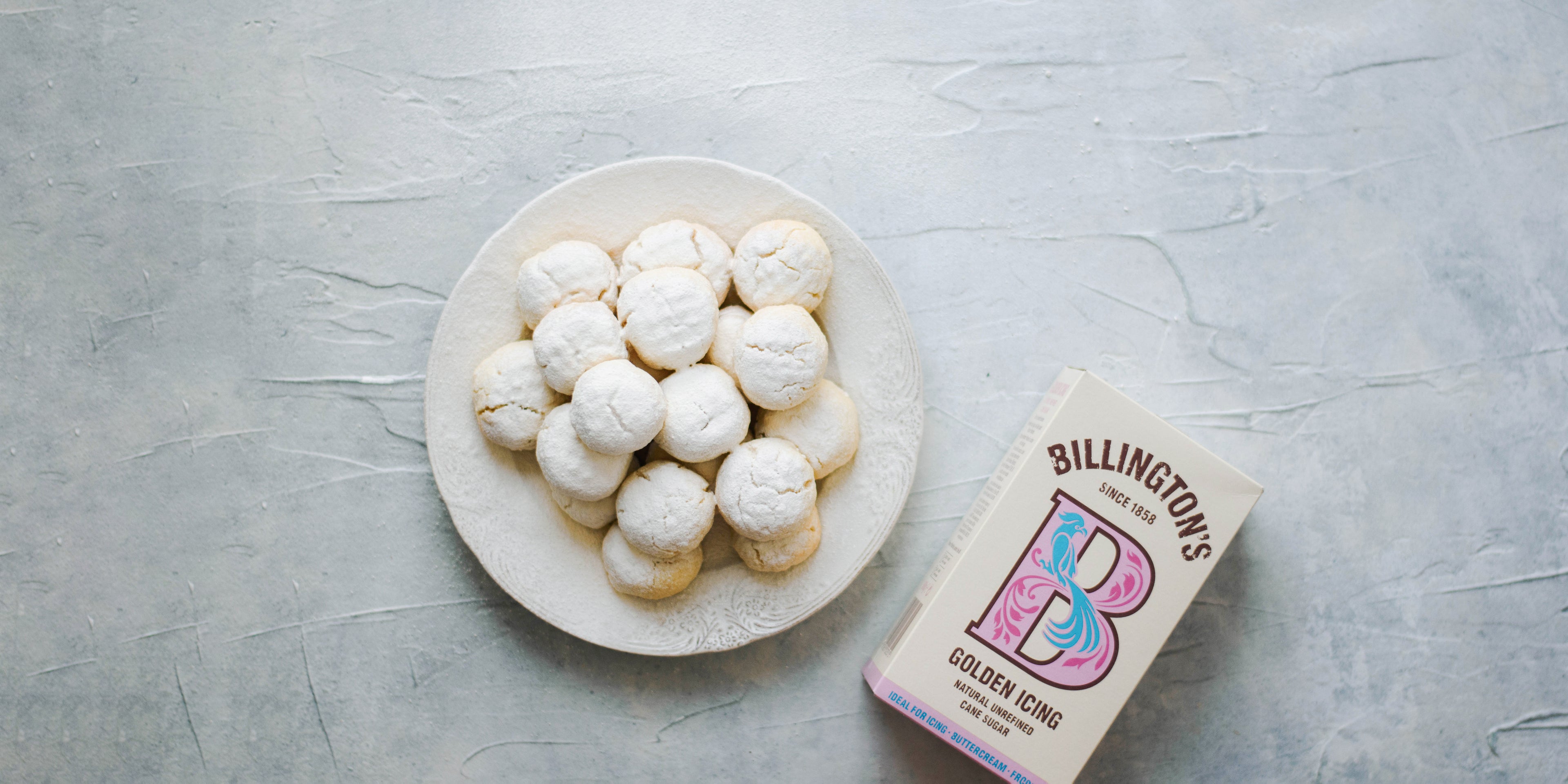 Kahk Eid dusted with golden icing sugar, next to a flat lay box of Billington's icing sugar