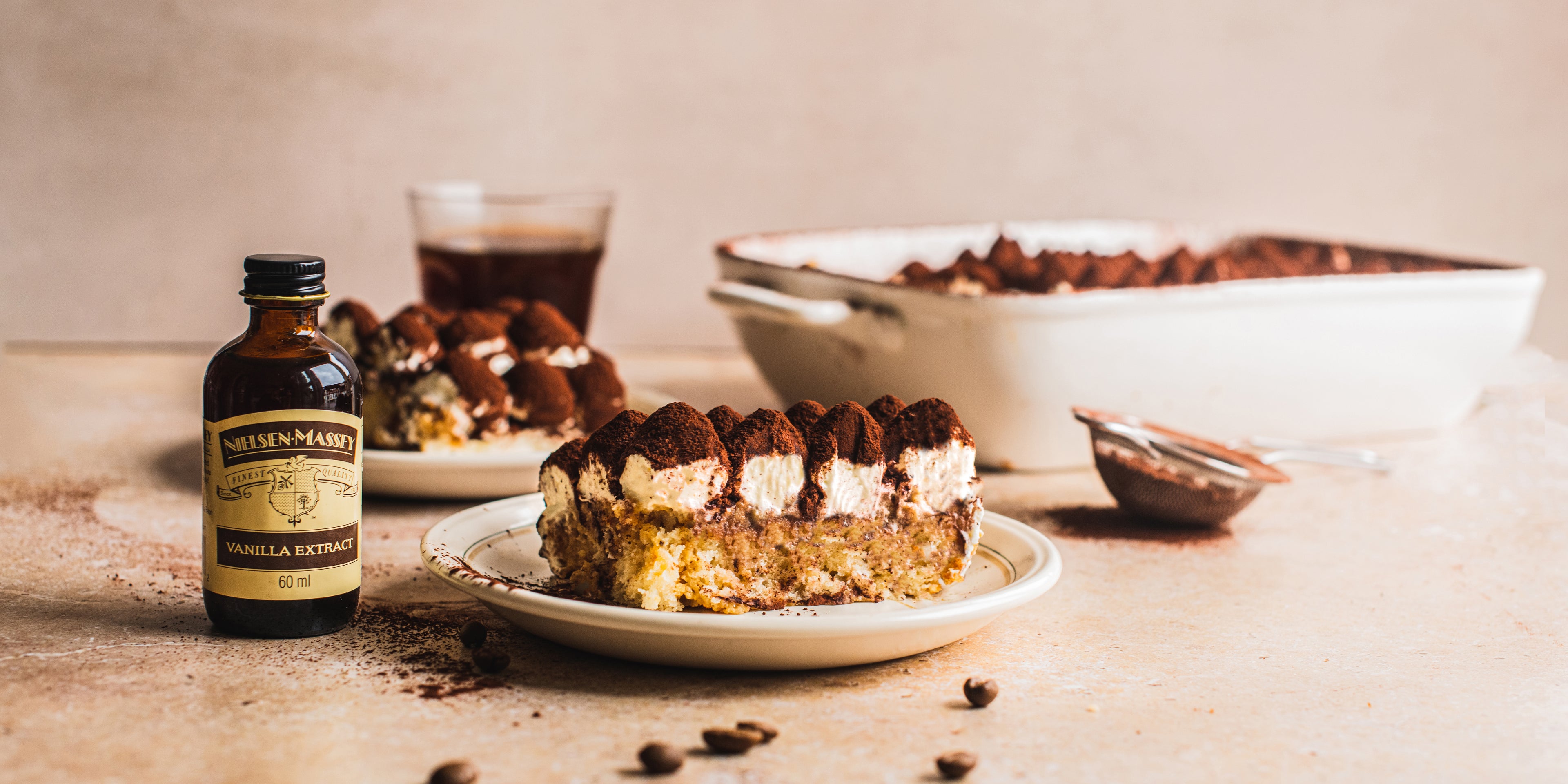 Vegan Tiramisu slice served on a place, next to a bottle of Nielsen-Massey vanilla extract