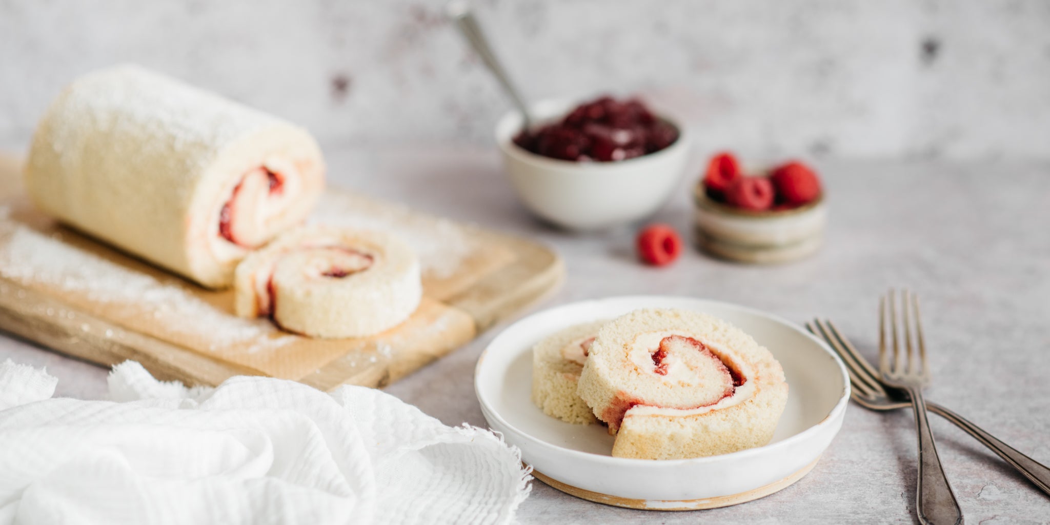 Two slices of vanilla swiss roll on a plate next to two forks