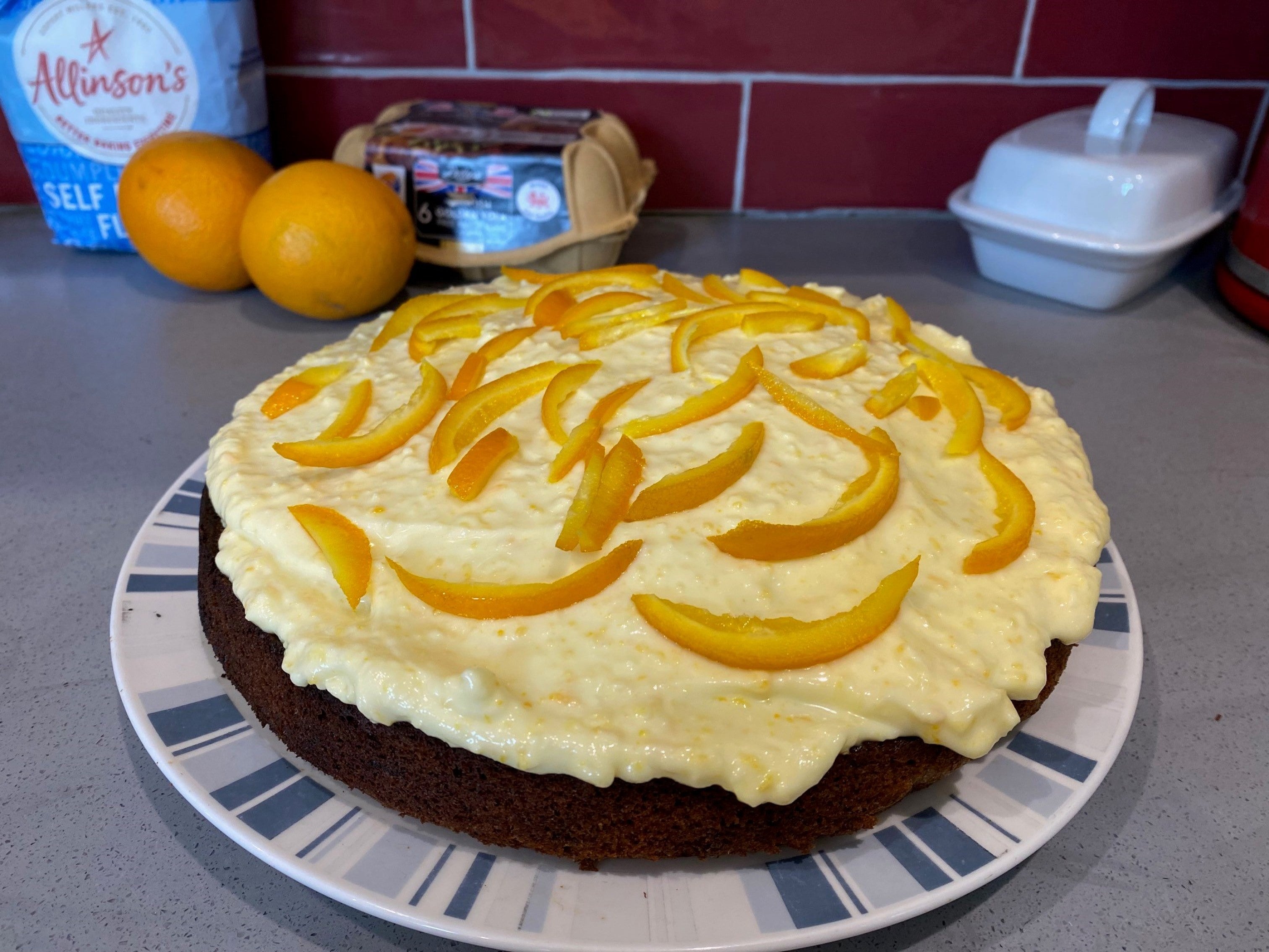 Paul Hollywood's carrot cake, made with orange buttercream, in front of a bag of flour and some eggs