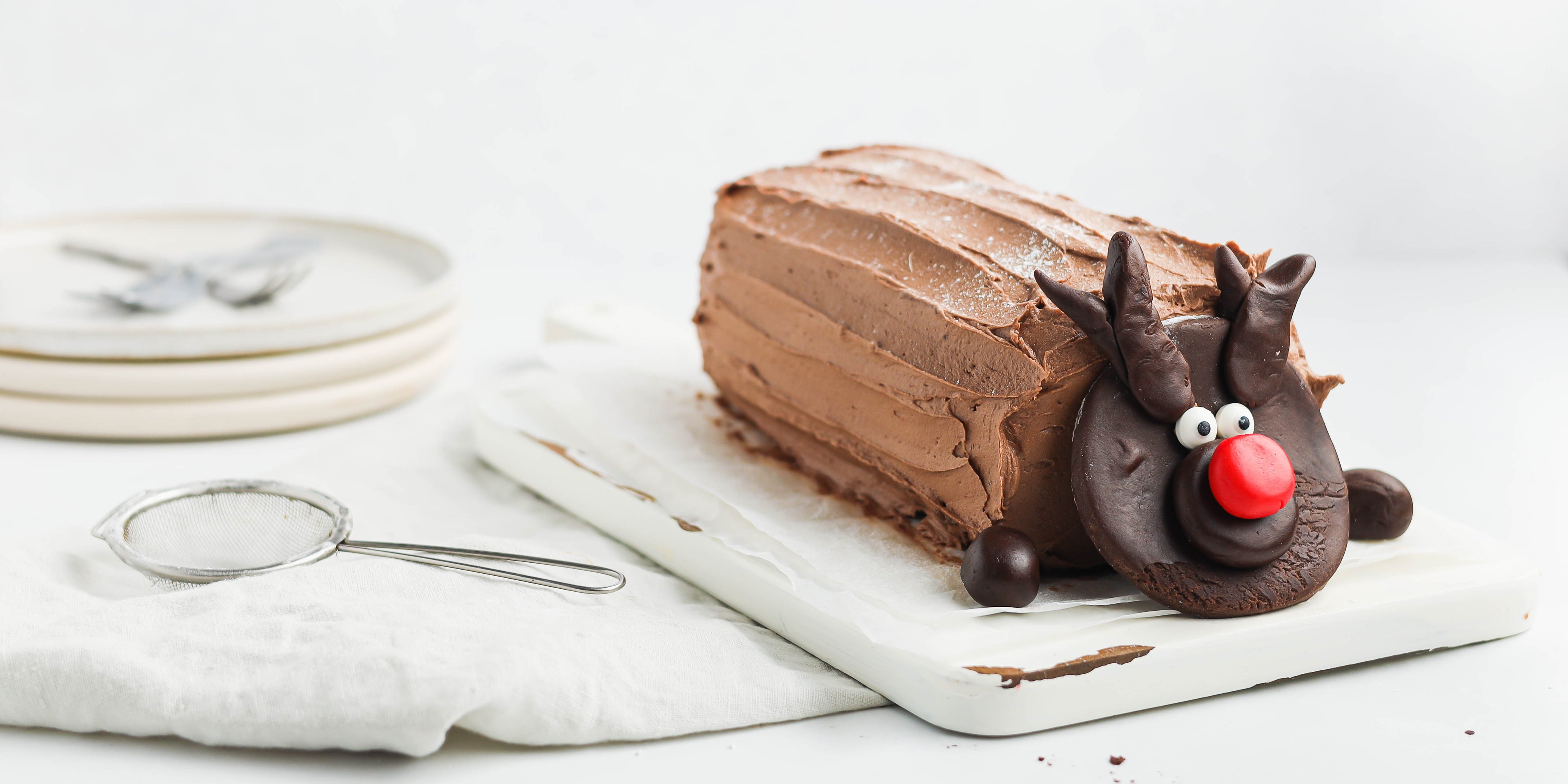 Chocolate Yule Log on a white chopping board with a chocolate reindeer face made from dark chocolate