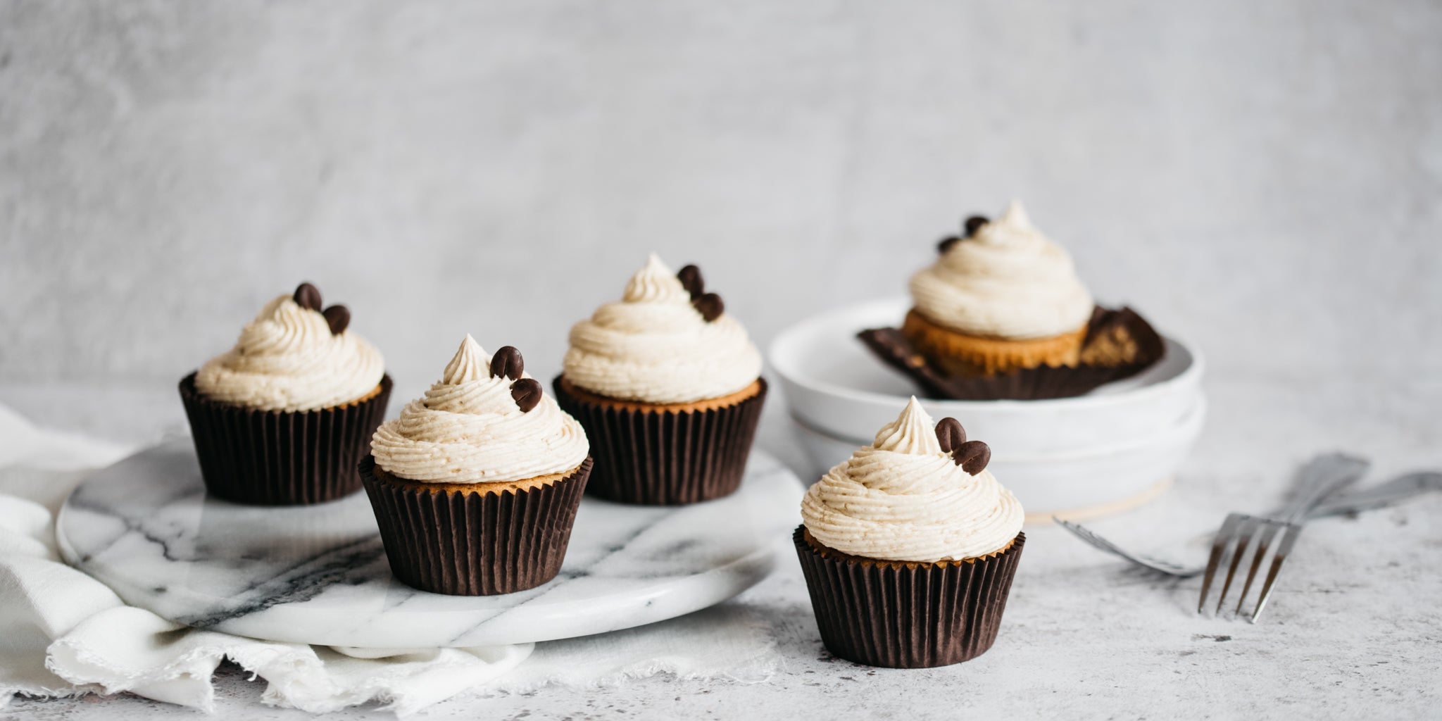 A fresh batch of coffee cupcakes whirled with coffee buttercream and coffee beans ready to serve on a marble cake board