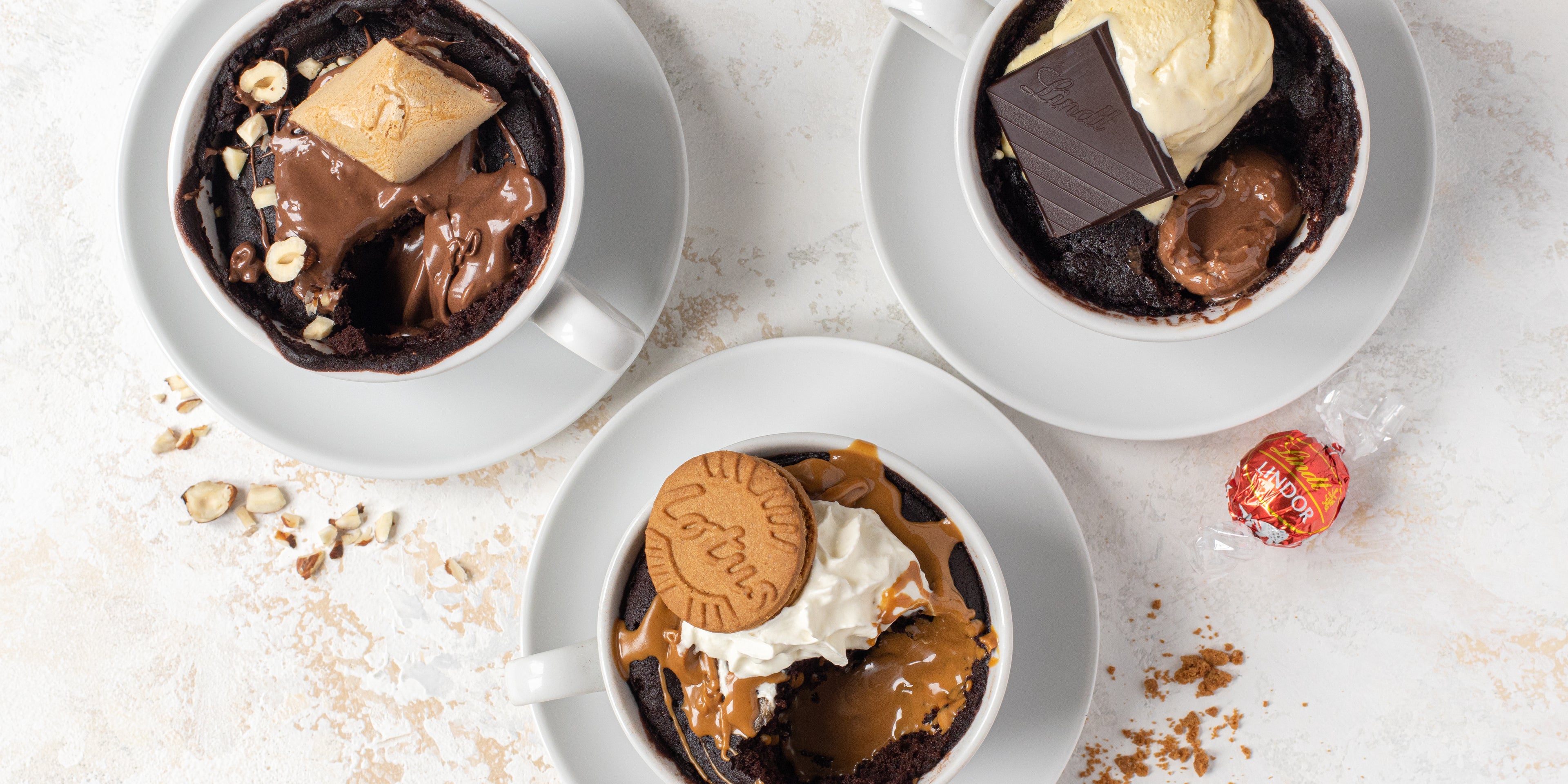 Top view of Chocolate Mug Cakes customised with Nutella, Lindt and Lotus Biscoff, with a Lindt ball and biscuit crumbs