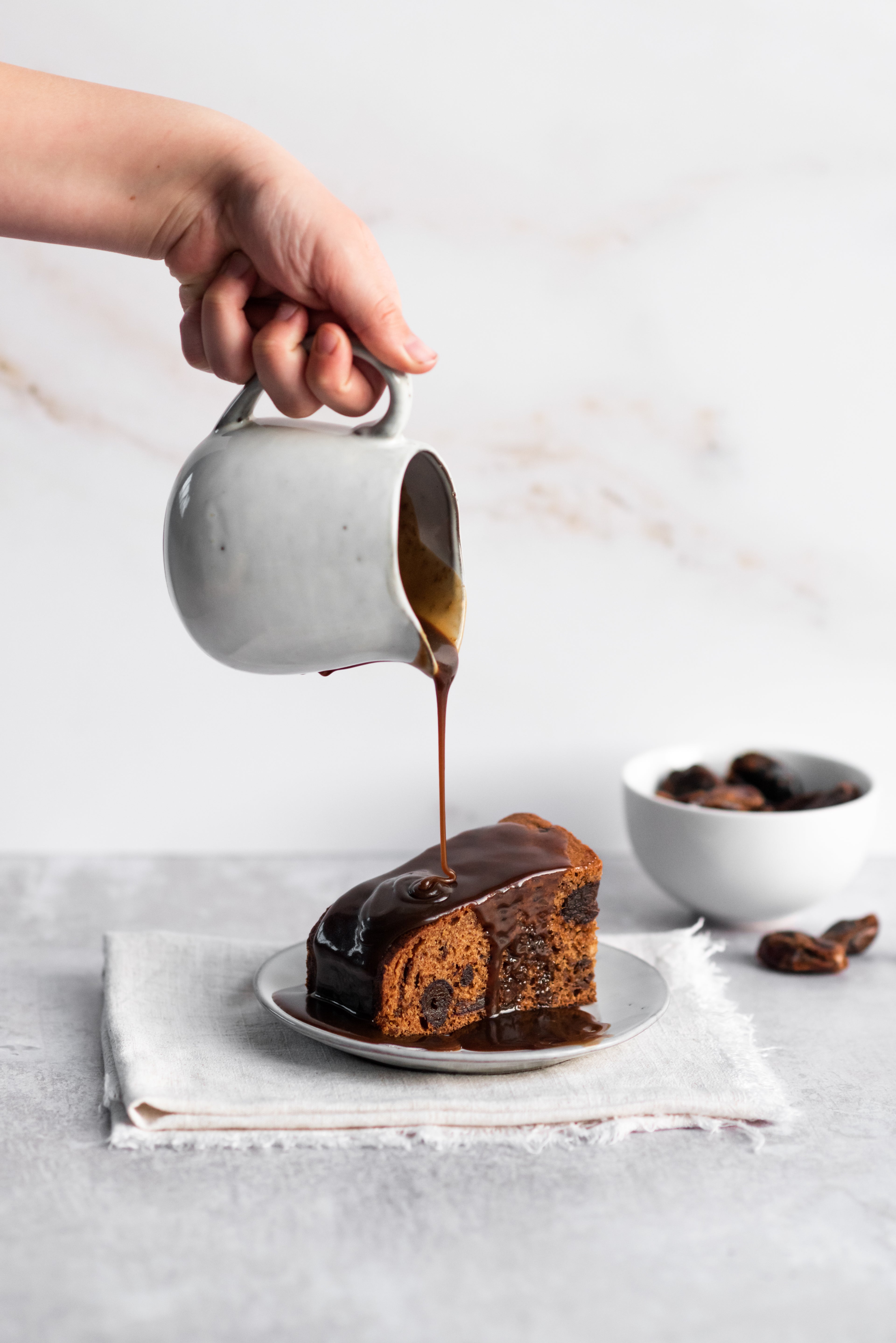 Plate of sticky toffee pudding and a hand pouring toffee sauce from a jug