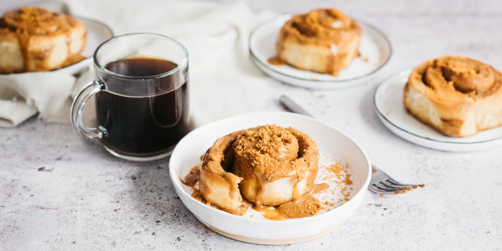 Cinnamon rolls with a creamy mocha topping next to a cup of black coffee
