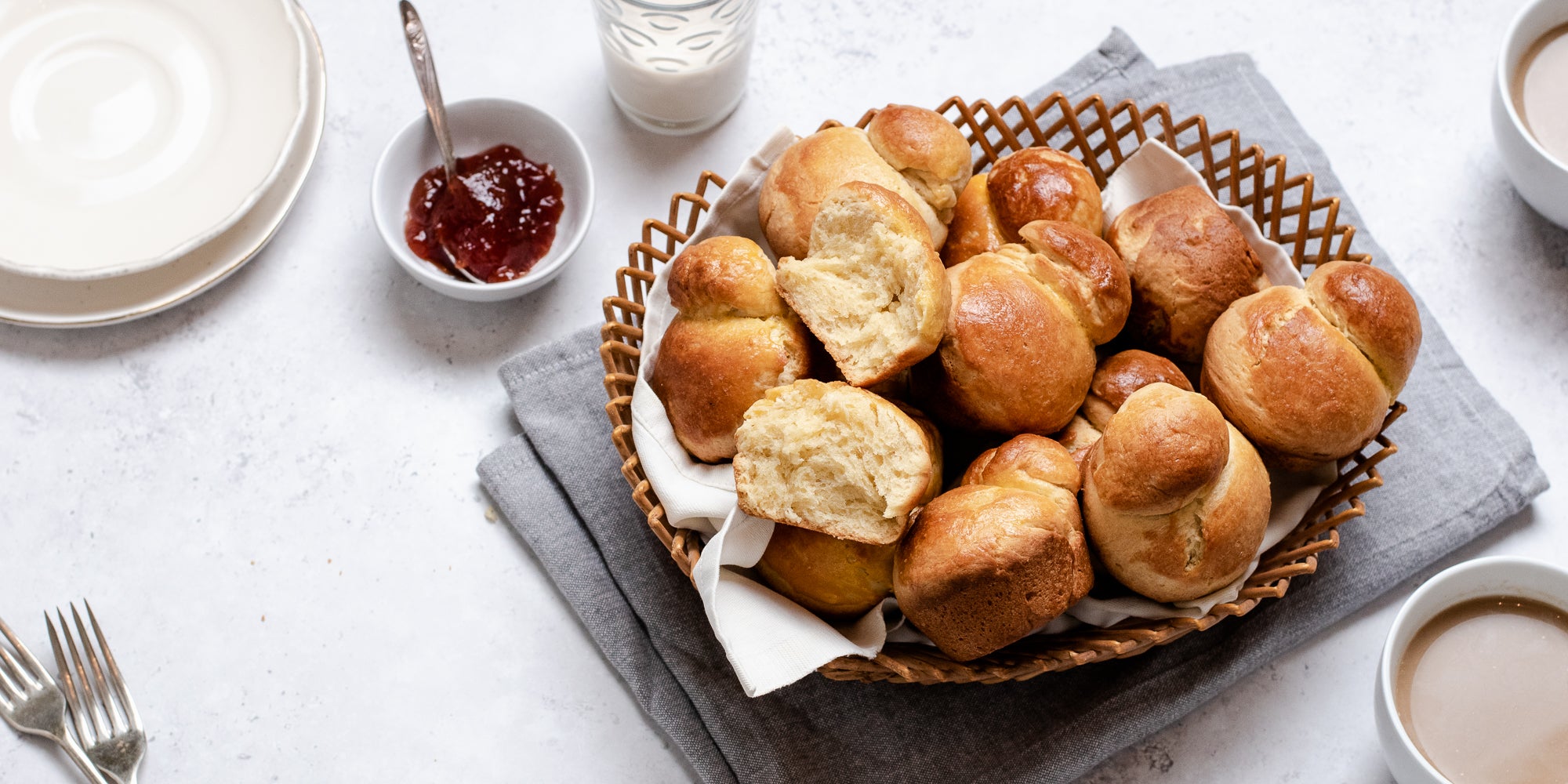 Basket of fresh Brioche, with one torn apart showing the fluffy inside. Next to a small bowl of jam with a spoon