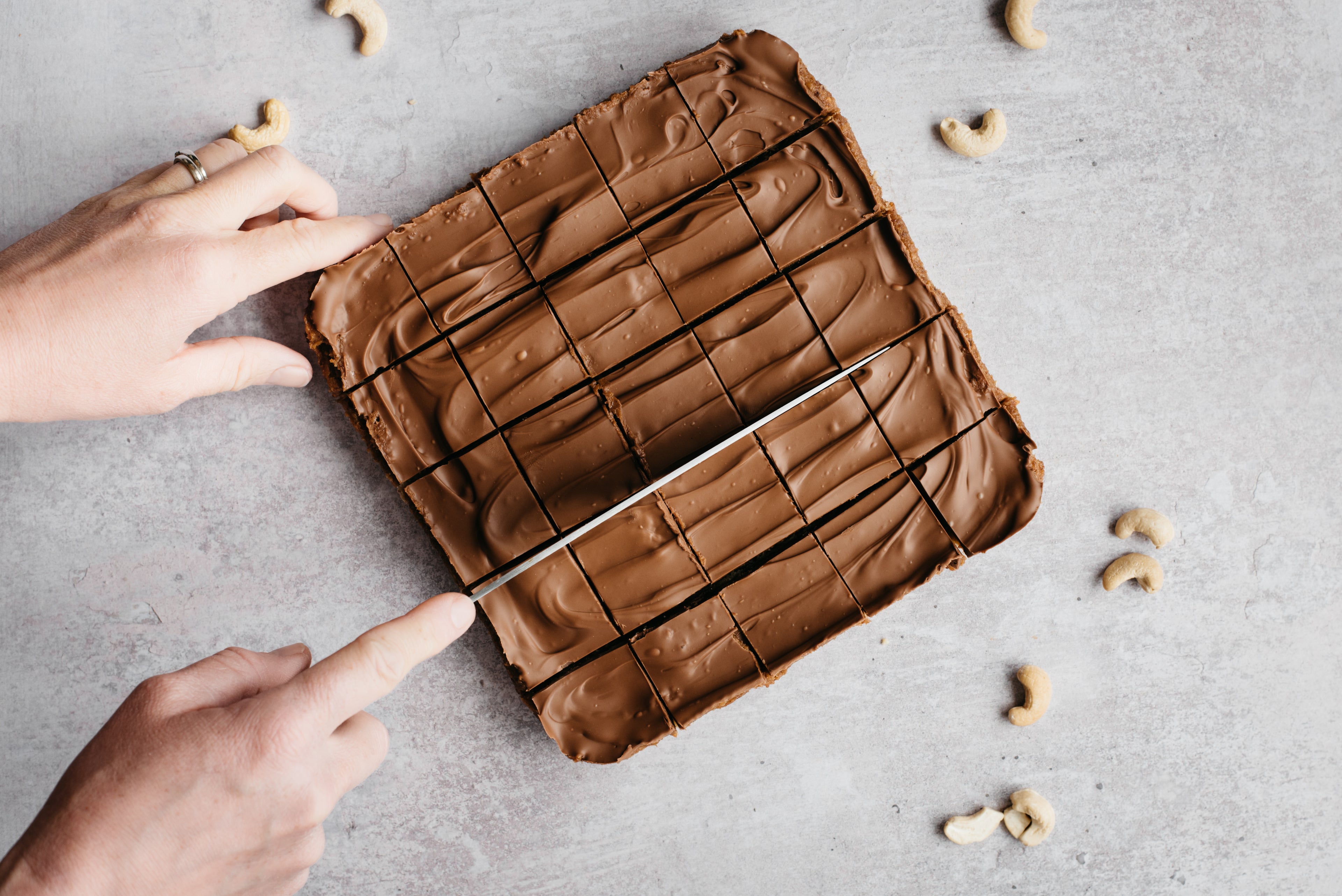 Top view of No-Bake Millionaire bites being cut into squares with a hand holding a knife