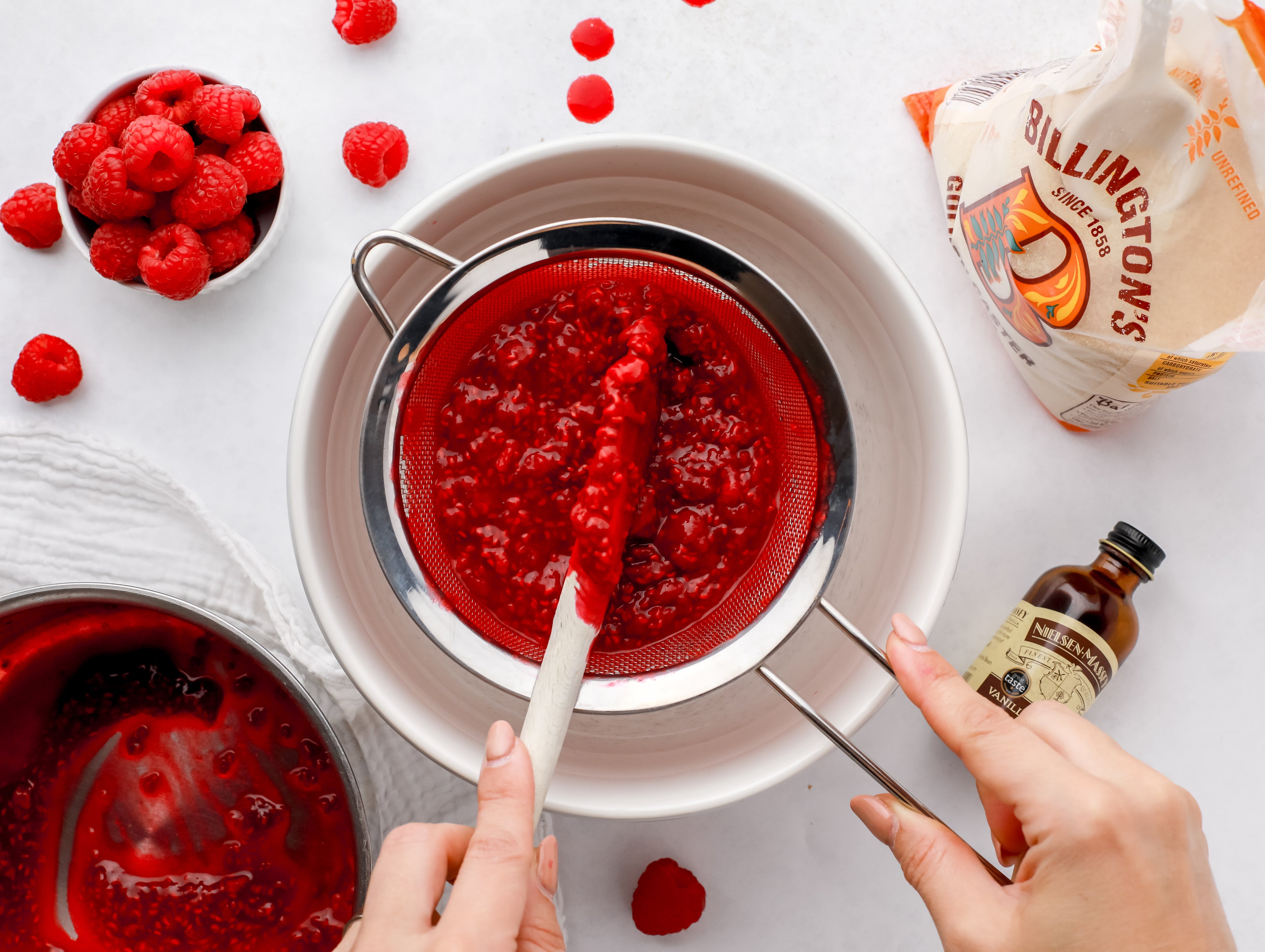 Raspberry coulis being passed through a sieve with a wooden spoon into a white bowl