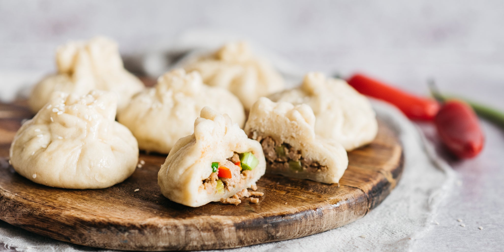 Bao buns on a circular wooden board one cut up showing the filling