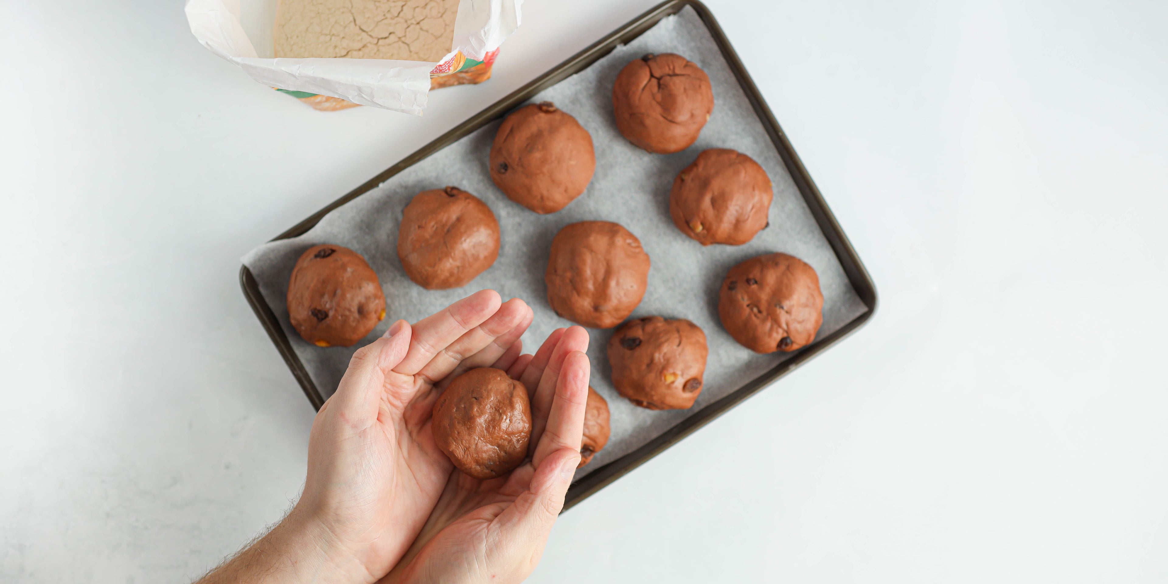 Chocolate Hot Cross Buns being shaped with hands and lay onto a baking tray ready to bake
