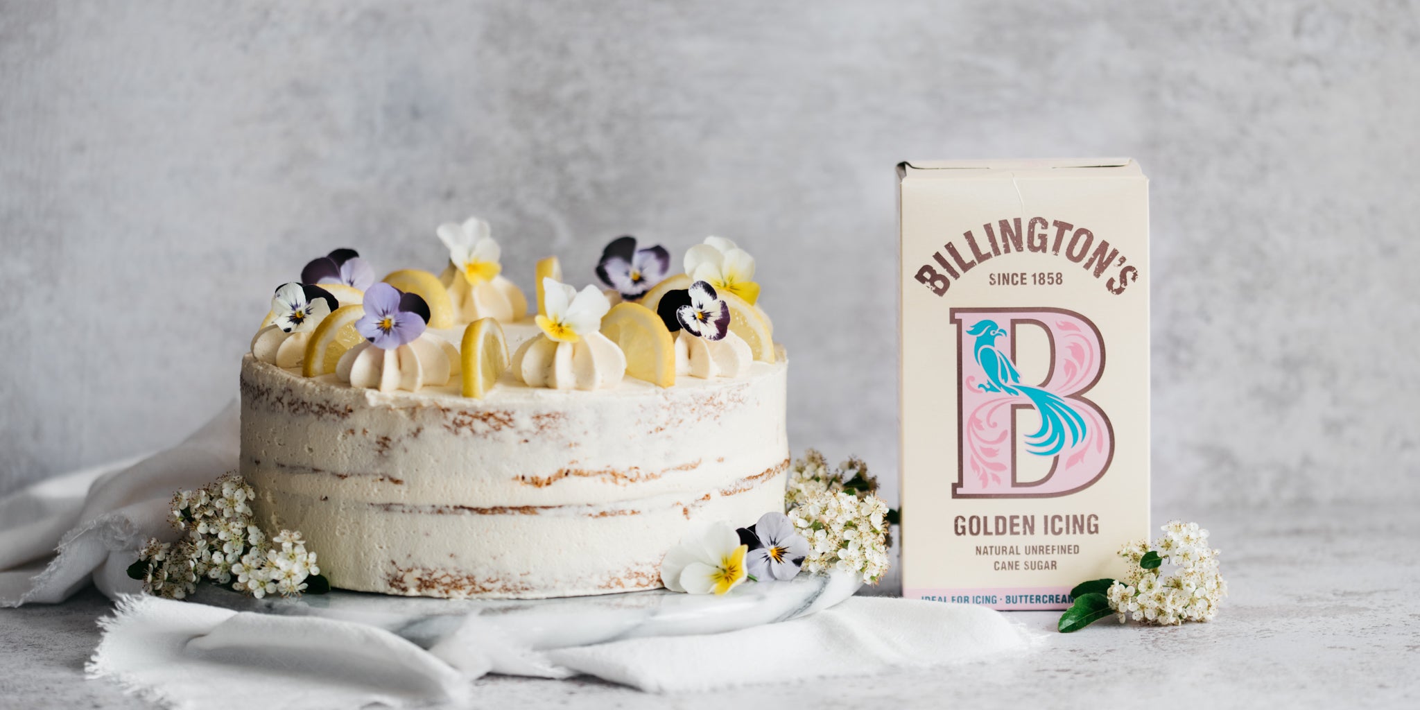 Cake topped with lemons and flowers beside a sugar pack