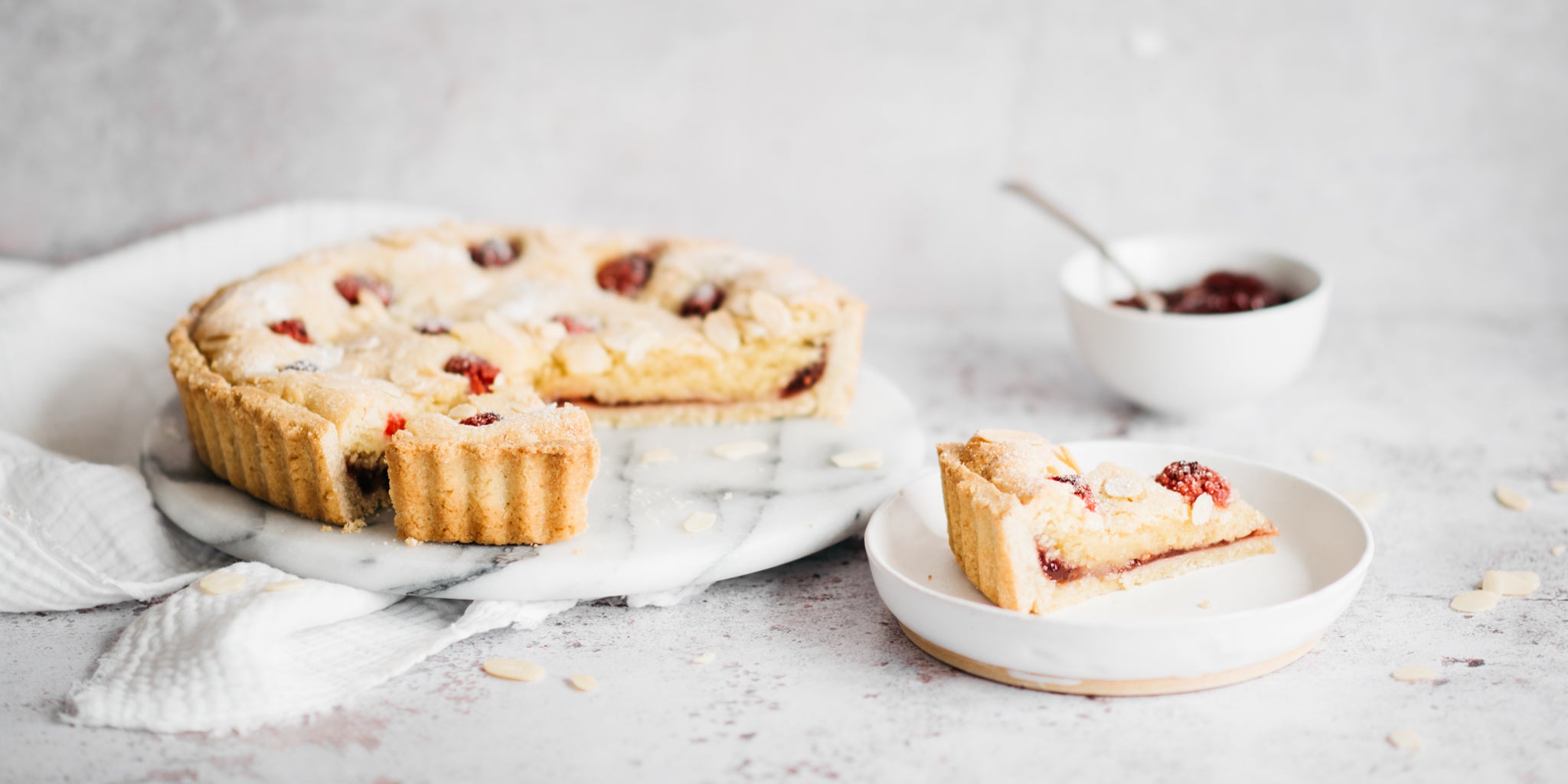 Bakewell tart on a white plate with a slice removed and positioned infront of it