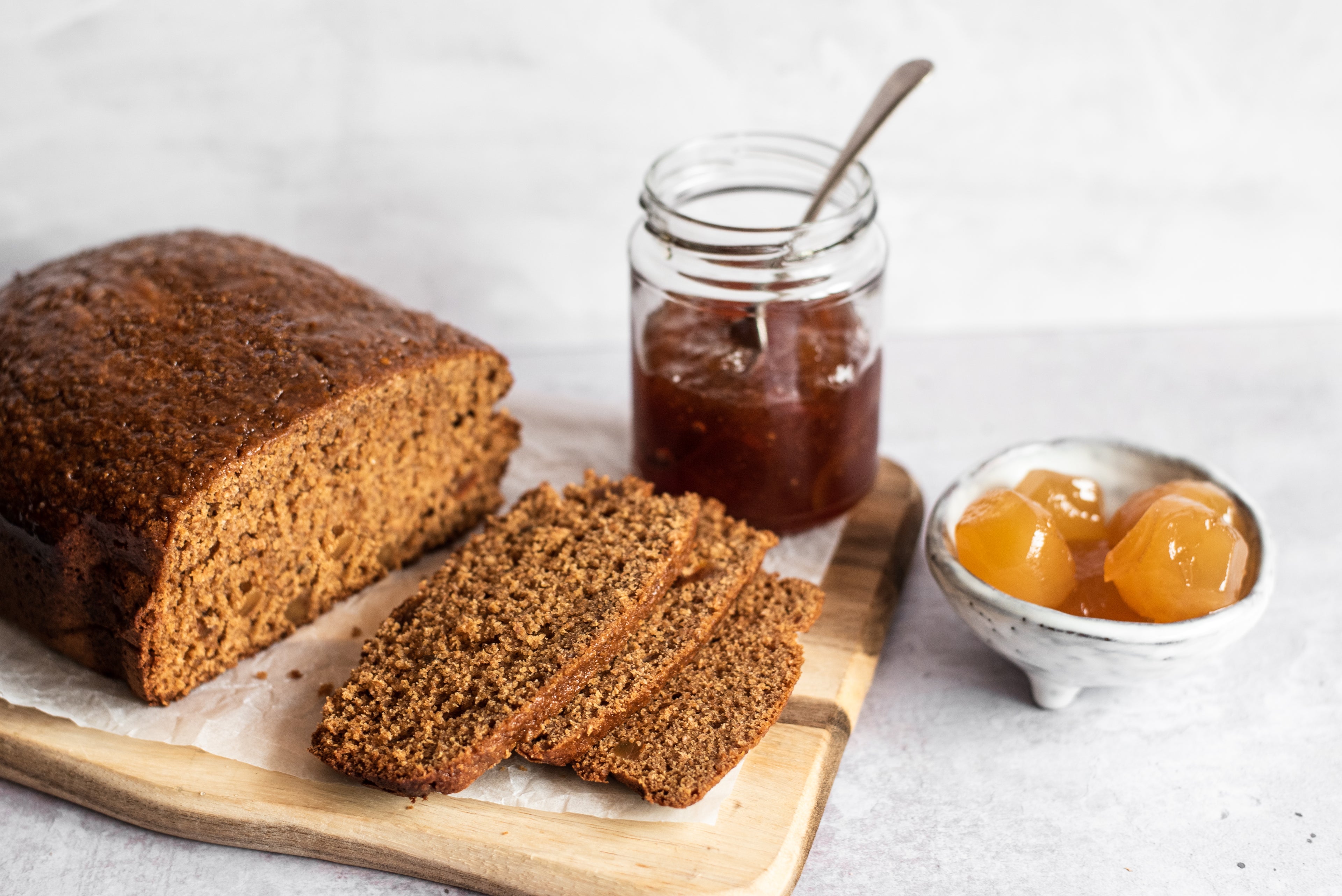Gingerbread loaf on bread board, three slices infront, ginger in bowl and marmalade