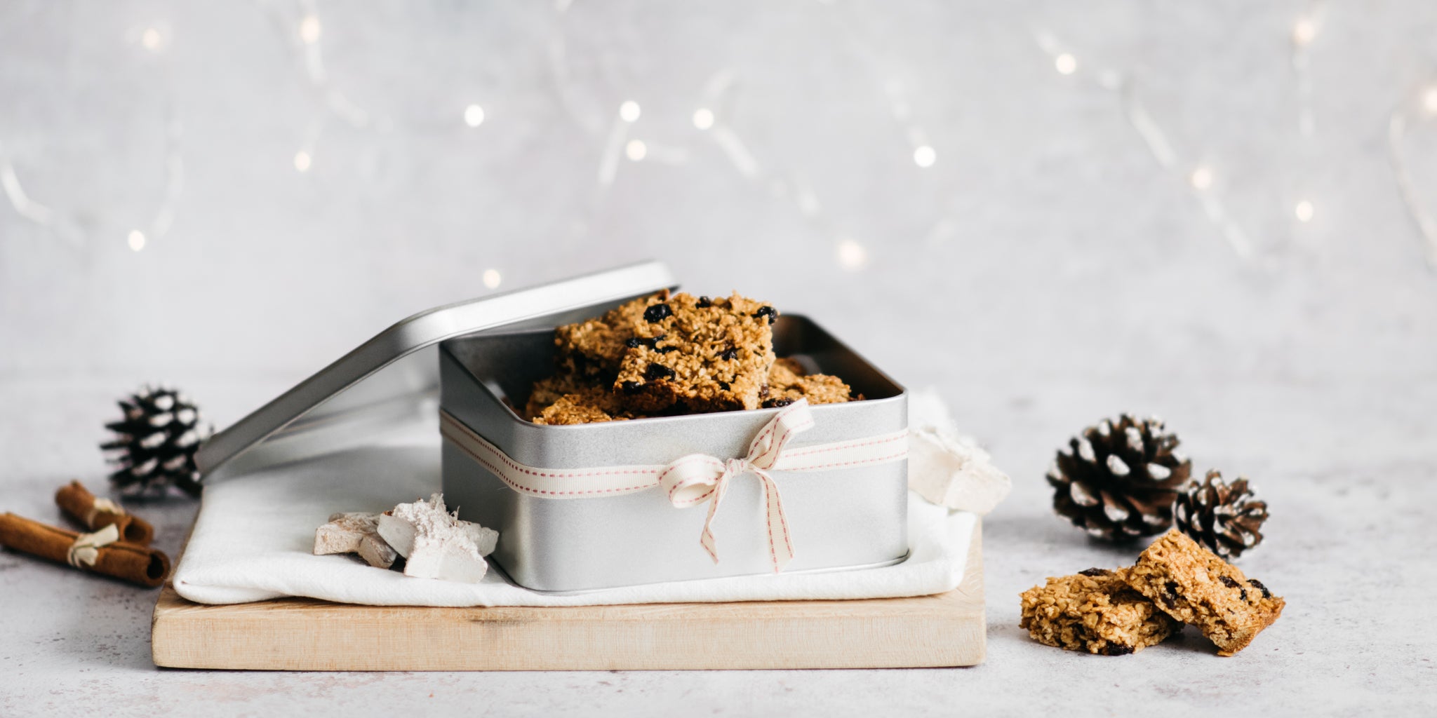 Flapjacks in a gifting tin with cinnamon sticks and pinecones beside it