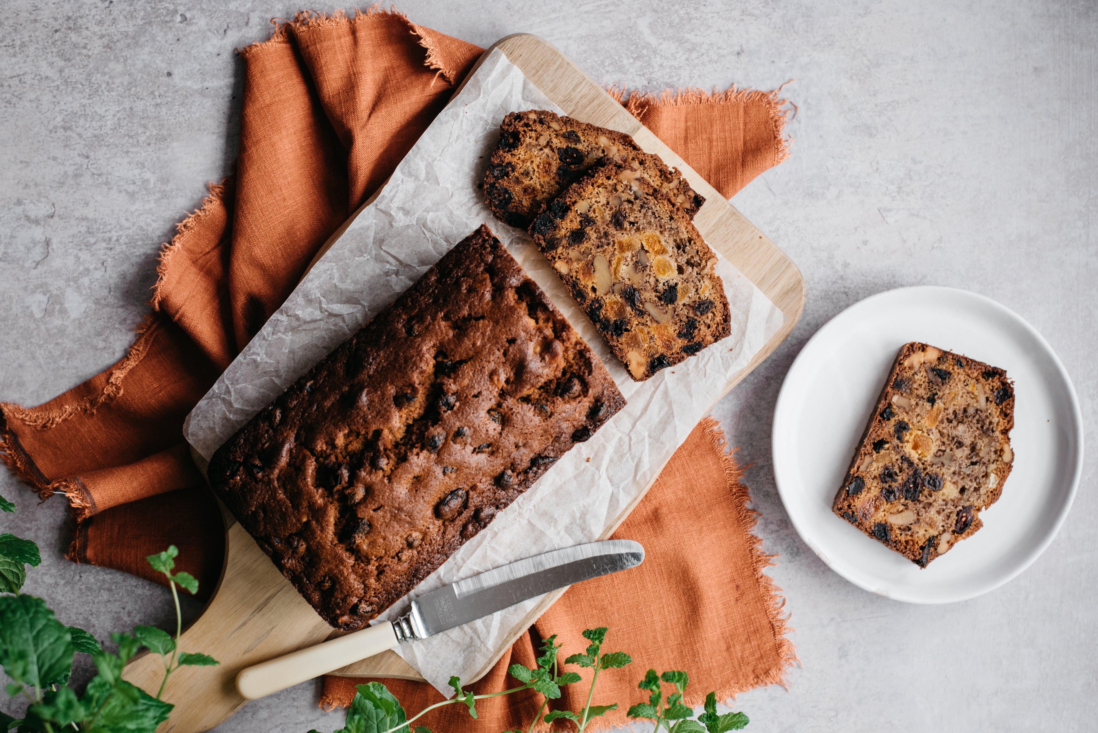 Top down view of a loaf of light fruit cake with a slice on a plate next to it