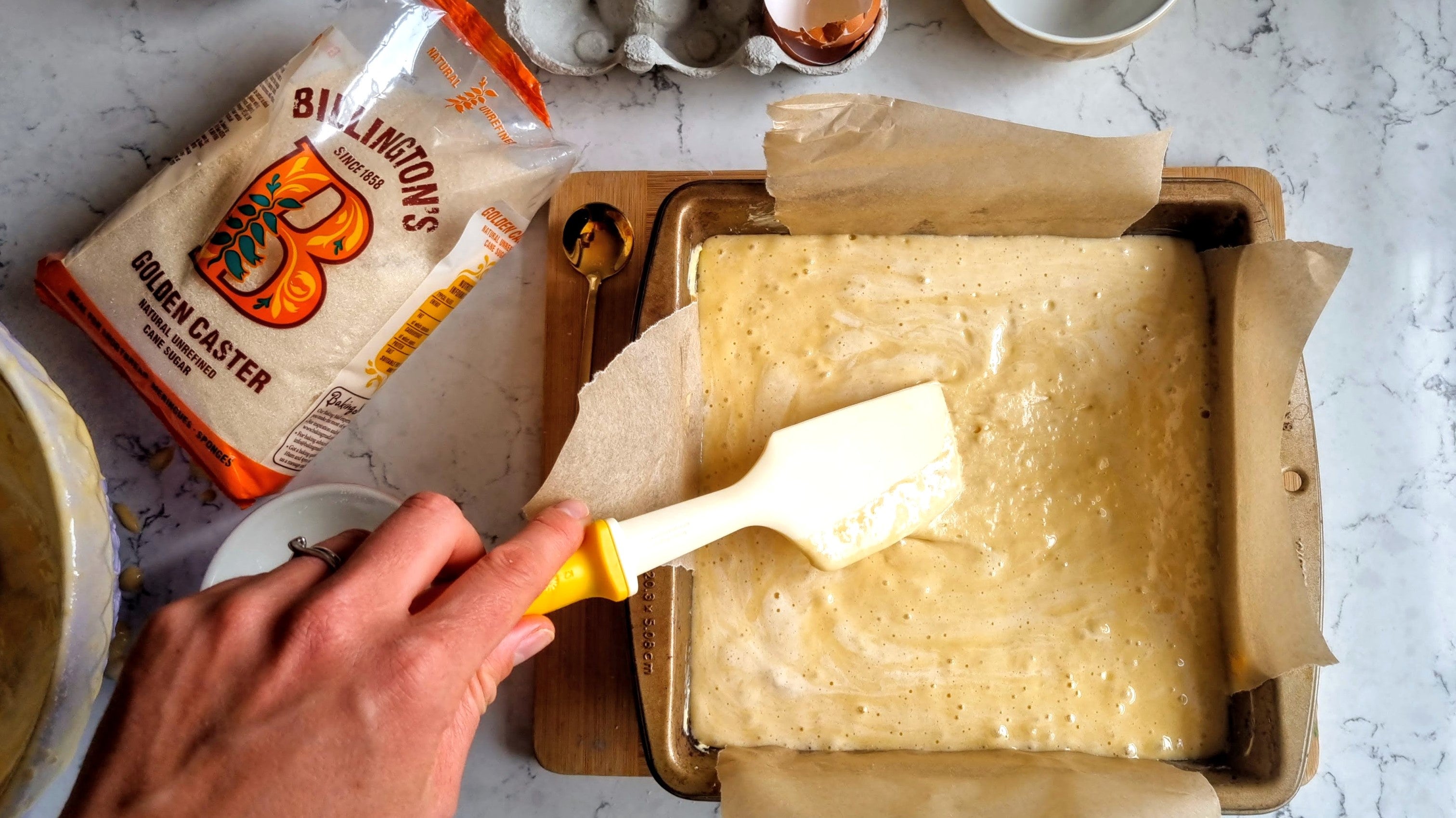 Smoothing down white chocolate brownie batter inside a square tin lined with parchment