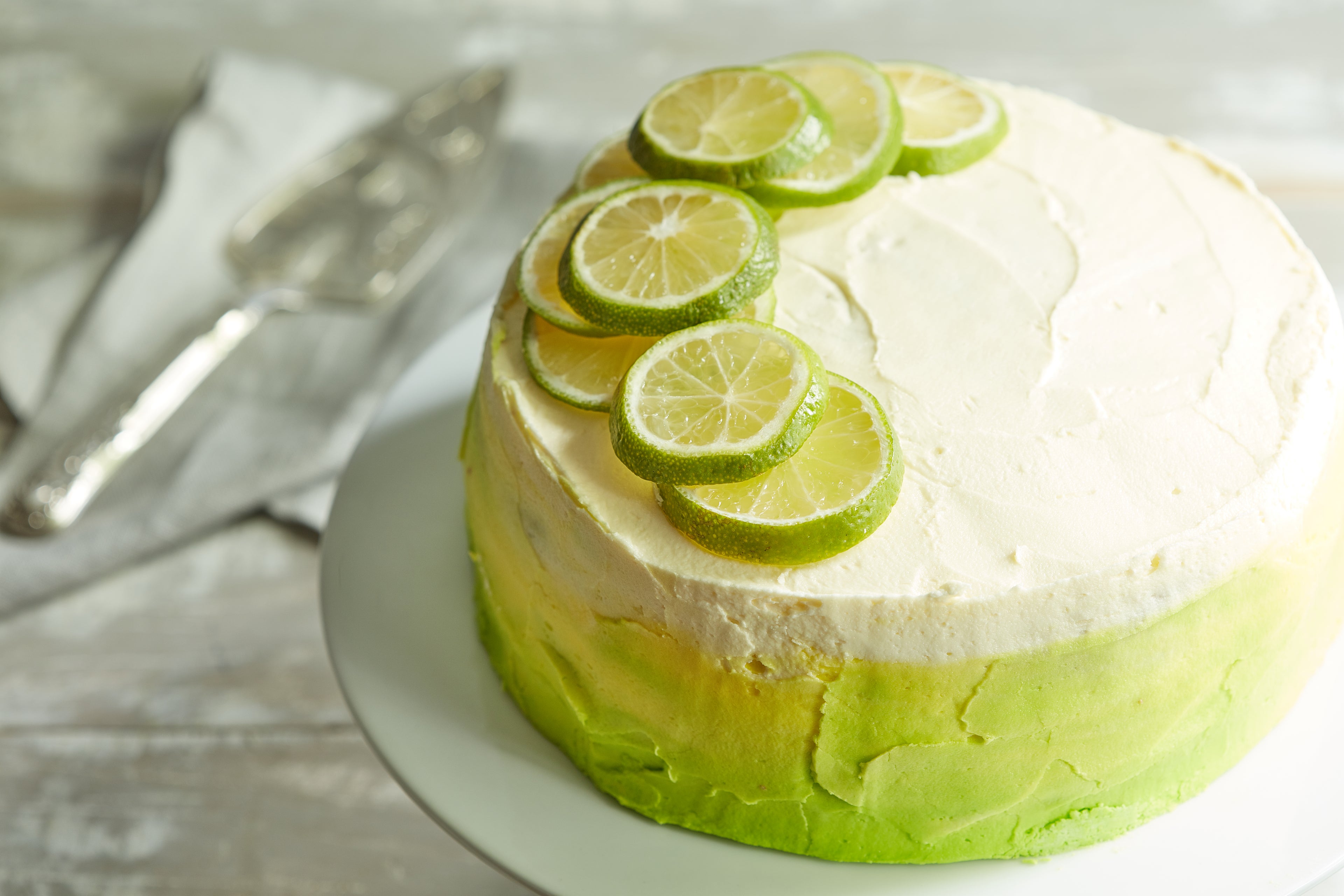Overhead image of cake covered in ombre white and green icing and topped with sliced limes