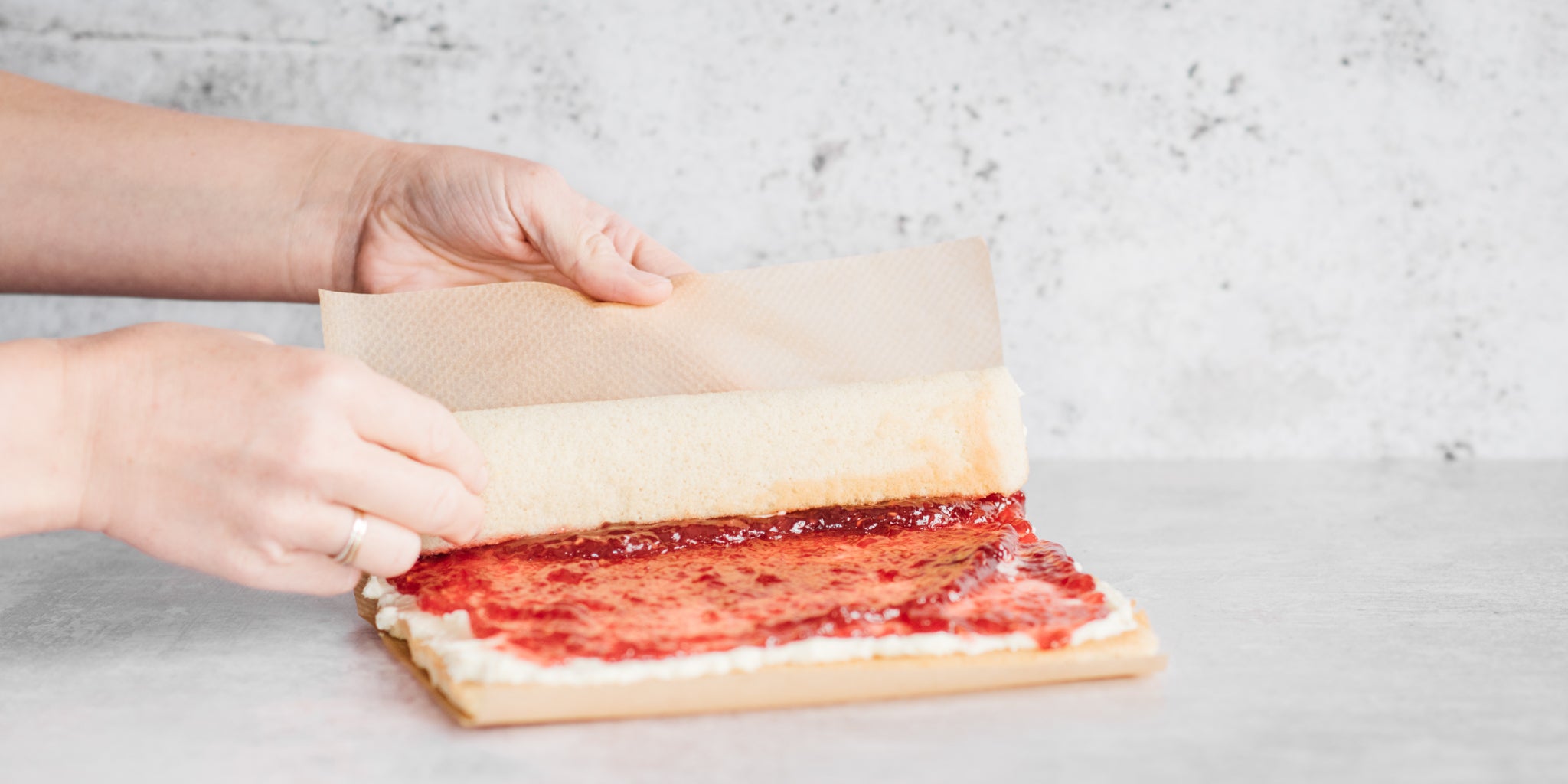 Hands rolling a vanilla swiss roll