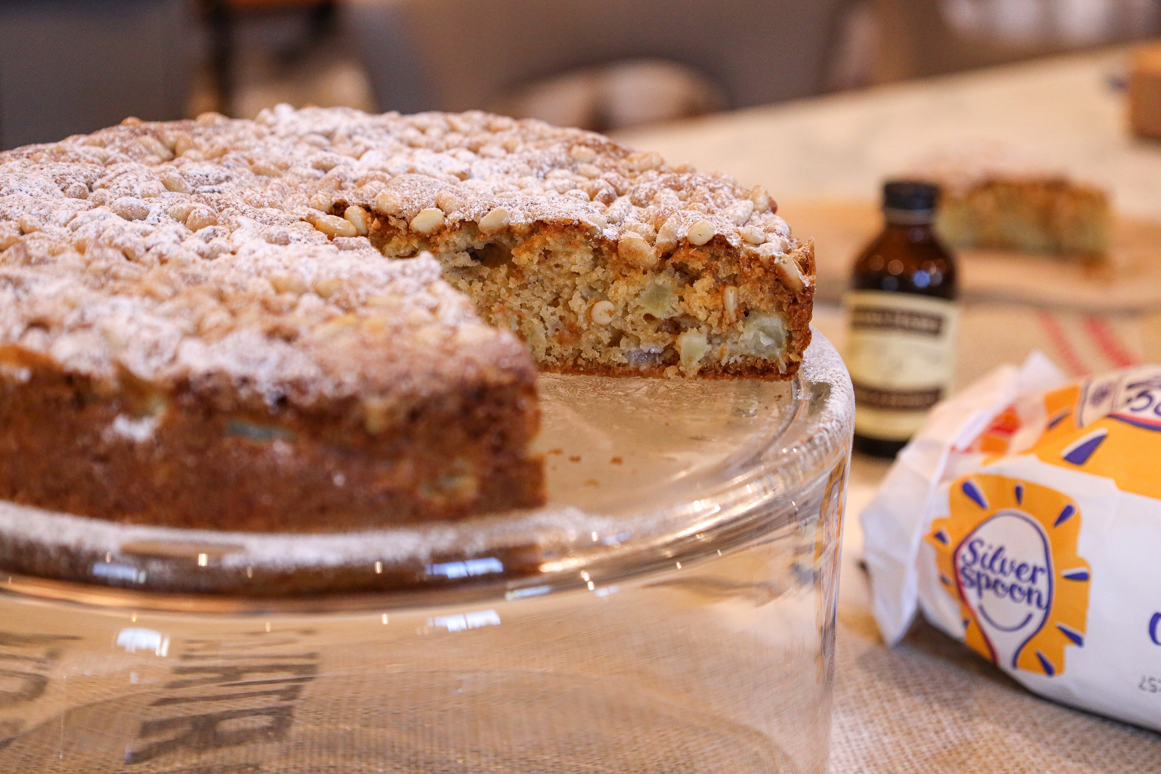 Apple cake with slice cut out, sugar pack and vanilla bottle in background
