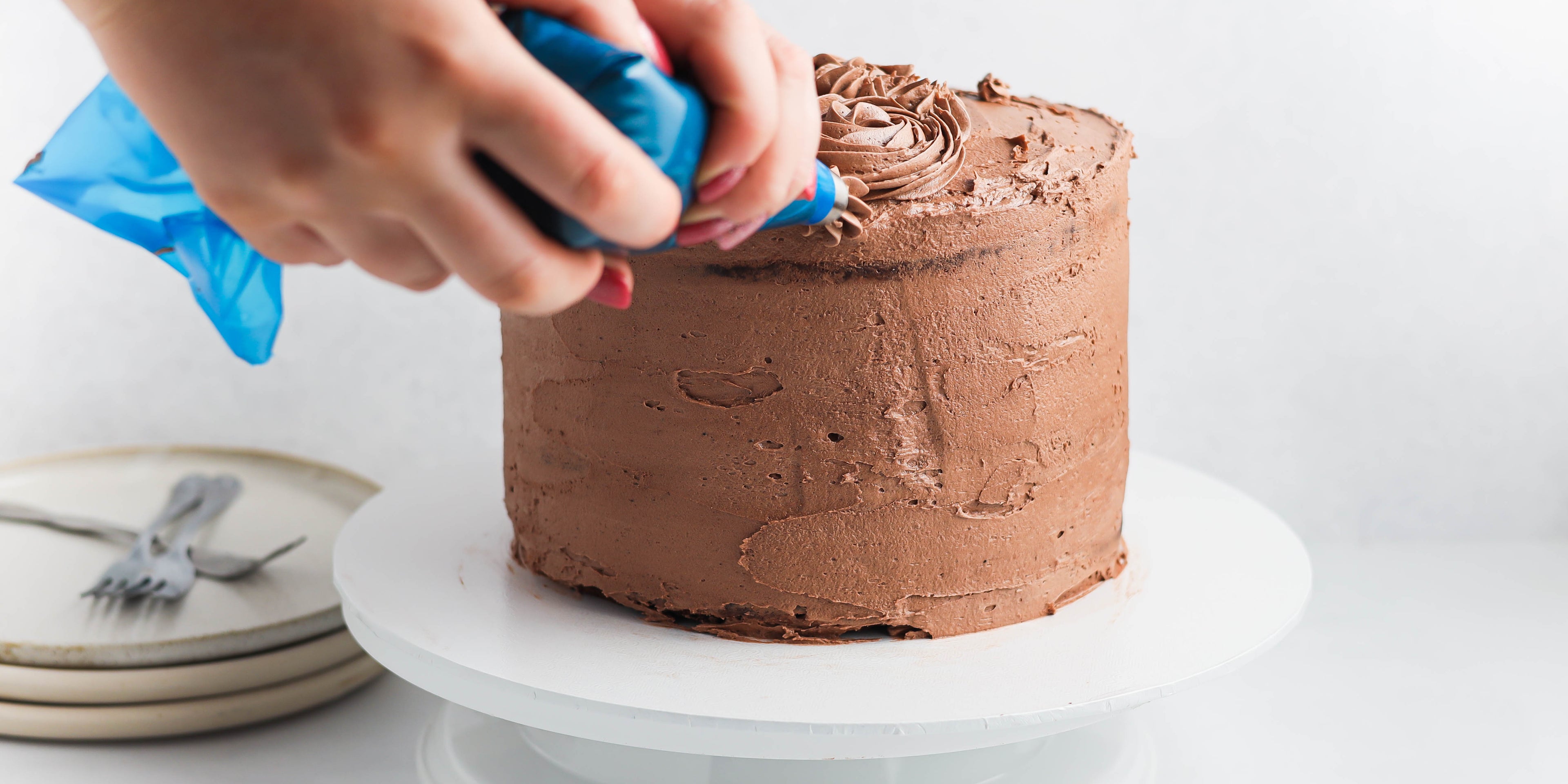 Christmas Reindeer Cake action shot, being piped with chocolate buttercream and a hand holding a piping bag