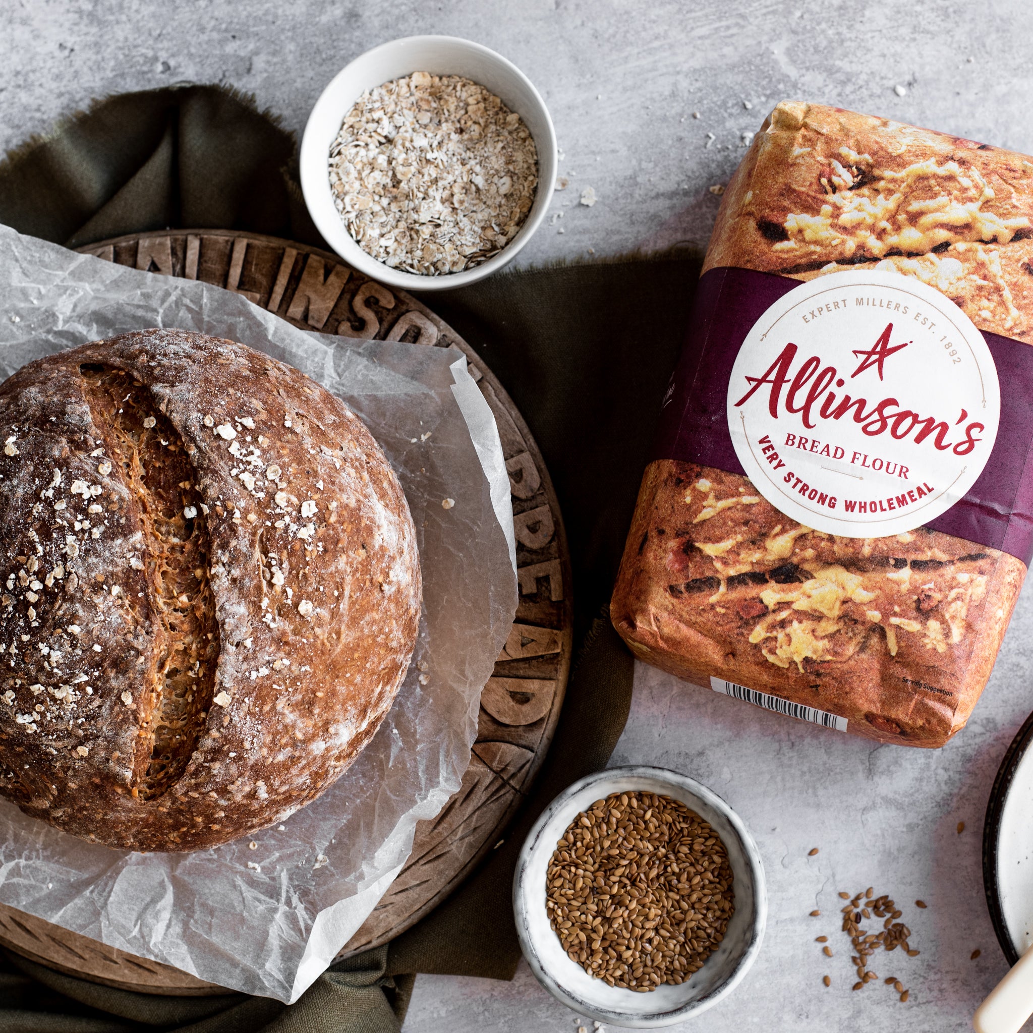 Overhead shot of round loaf of bread on bread board. Two bowls of linseed and bread flour