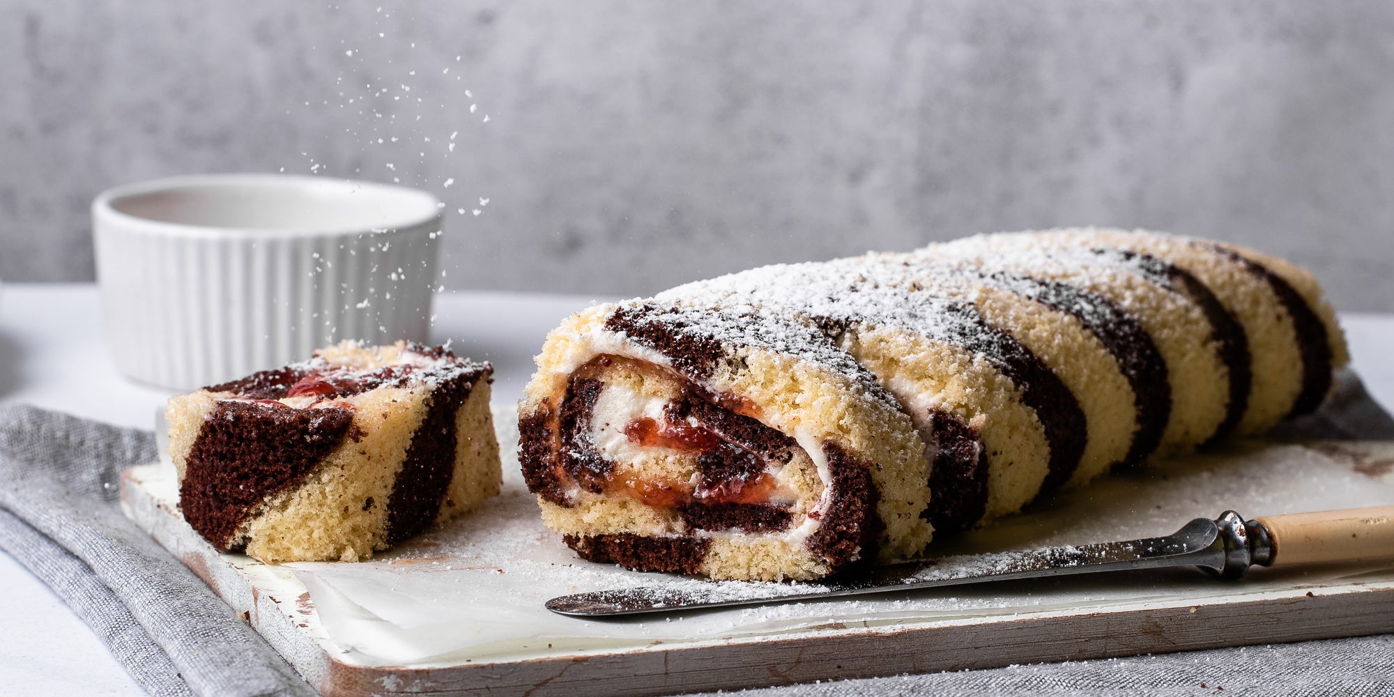 Chocolate & Vanilla Swiss Roll dusted in icing sugar, served on a wooden board