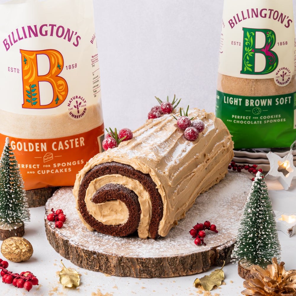 Biscoff Yule Log Cake with festive decorations on a wooden plinth next to two bags of Billington's sugars.