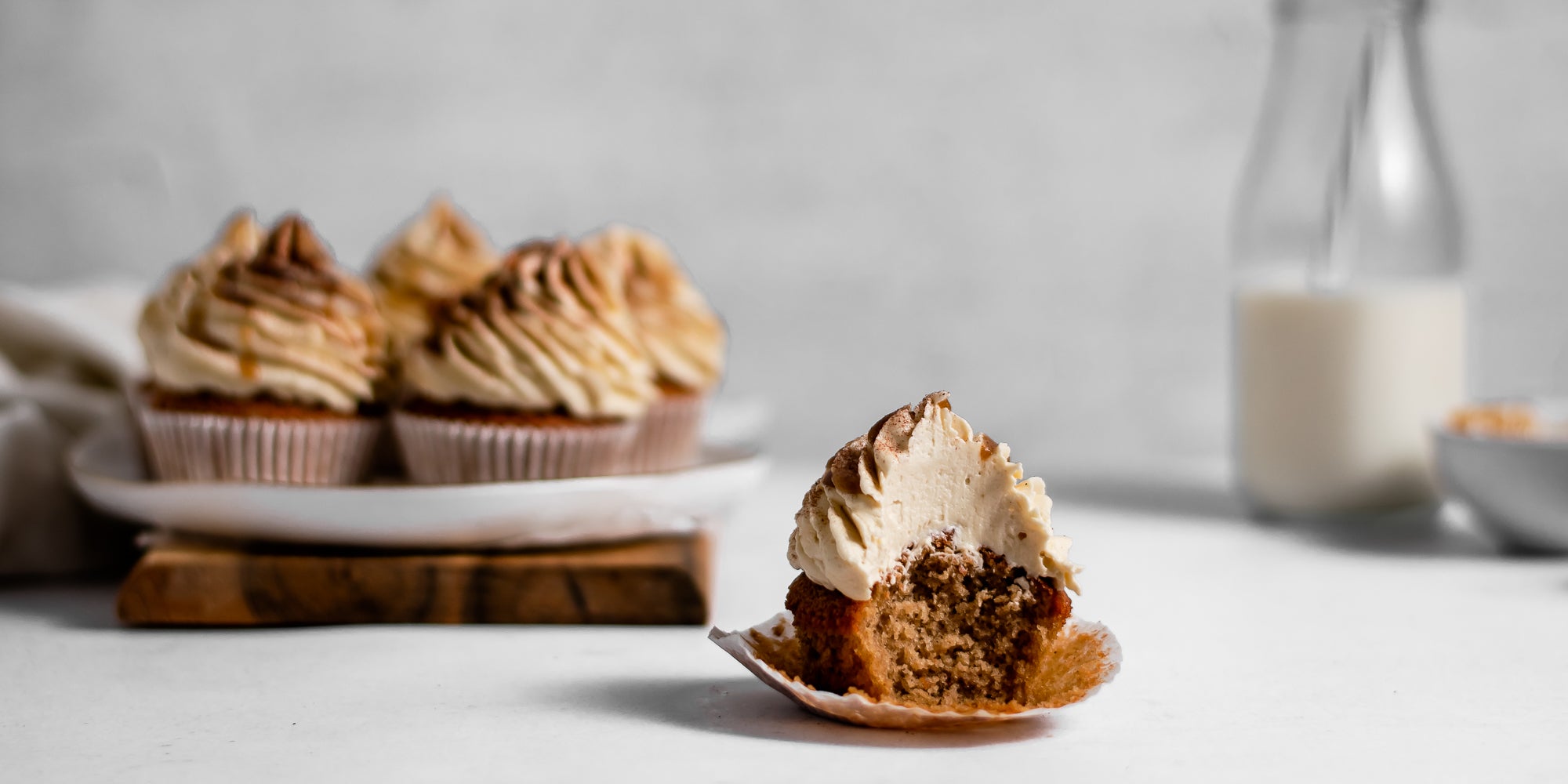 close up of Gingerbread Cinnamon Cupcake with a bite taken out of it showing the yummy insides. Batch of Gingerbread Cinnamon Cupcakes the background