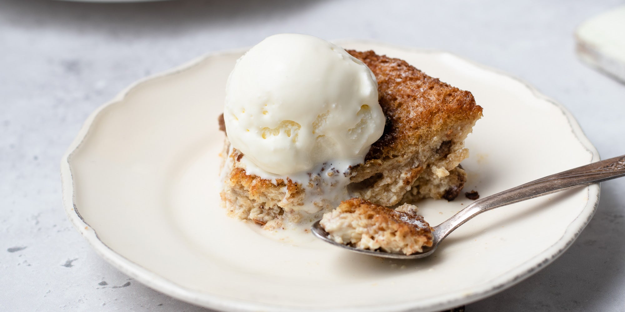 Close up of bread and butter pudding with spoon on white plate with scoop of ice cream 