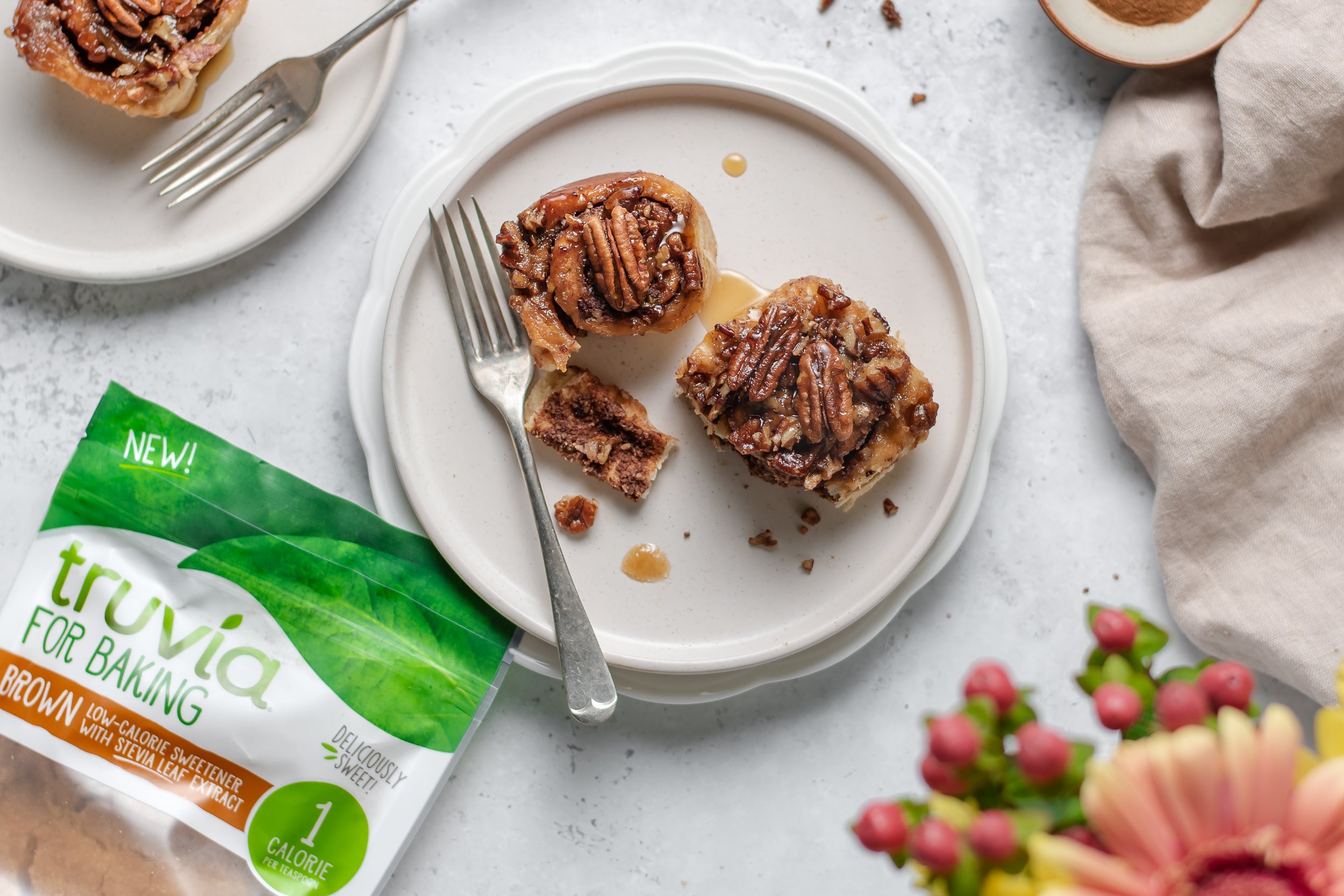 Low Sugar Sticky Pecan Buns top view, with a piece cut out of the bun, drizzled in sticky sauce next to a bag of Truvia for Baking Brown Sweetener