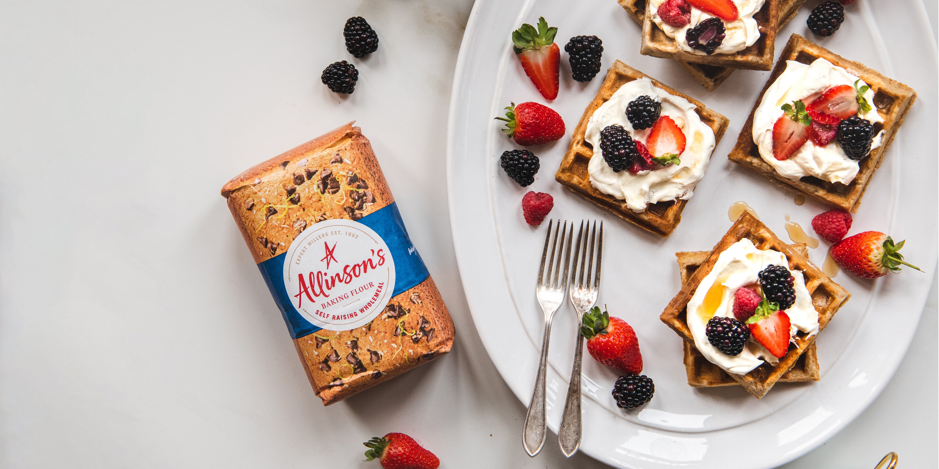 Top view of Wholemeal Banana Waffles next to a bag of Allinson's Flour, topped with cream and seasonal berries