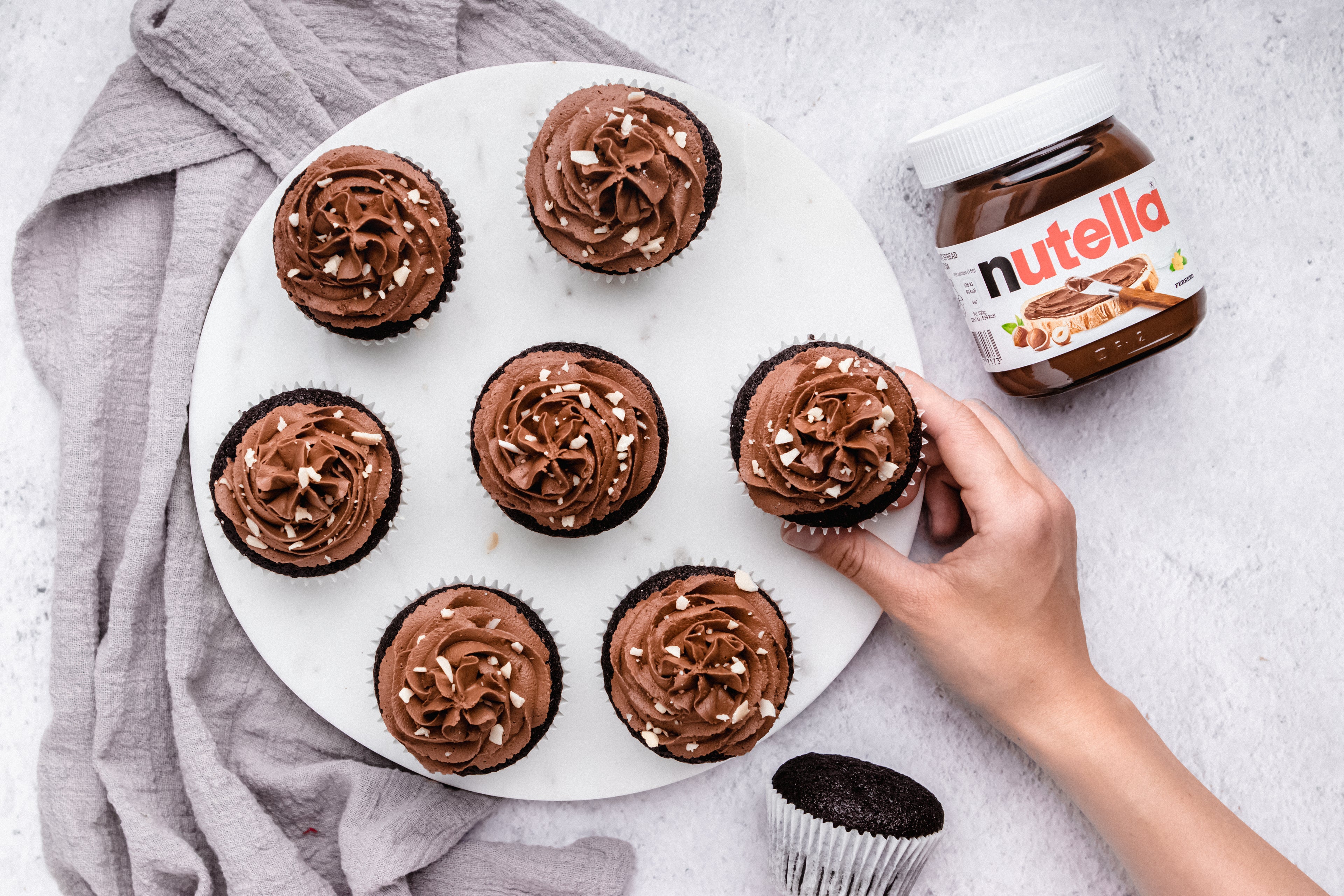 Nutella Cupcakes from above, with hand holding a cupcake next to a jar of Nutella