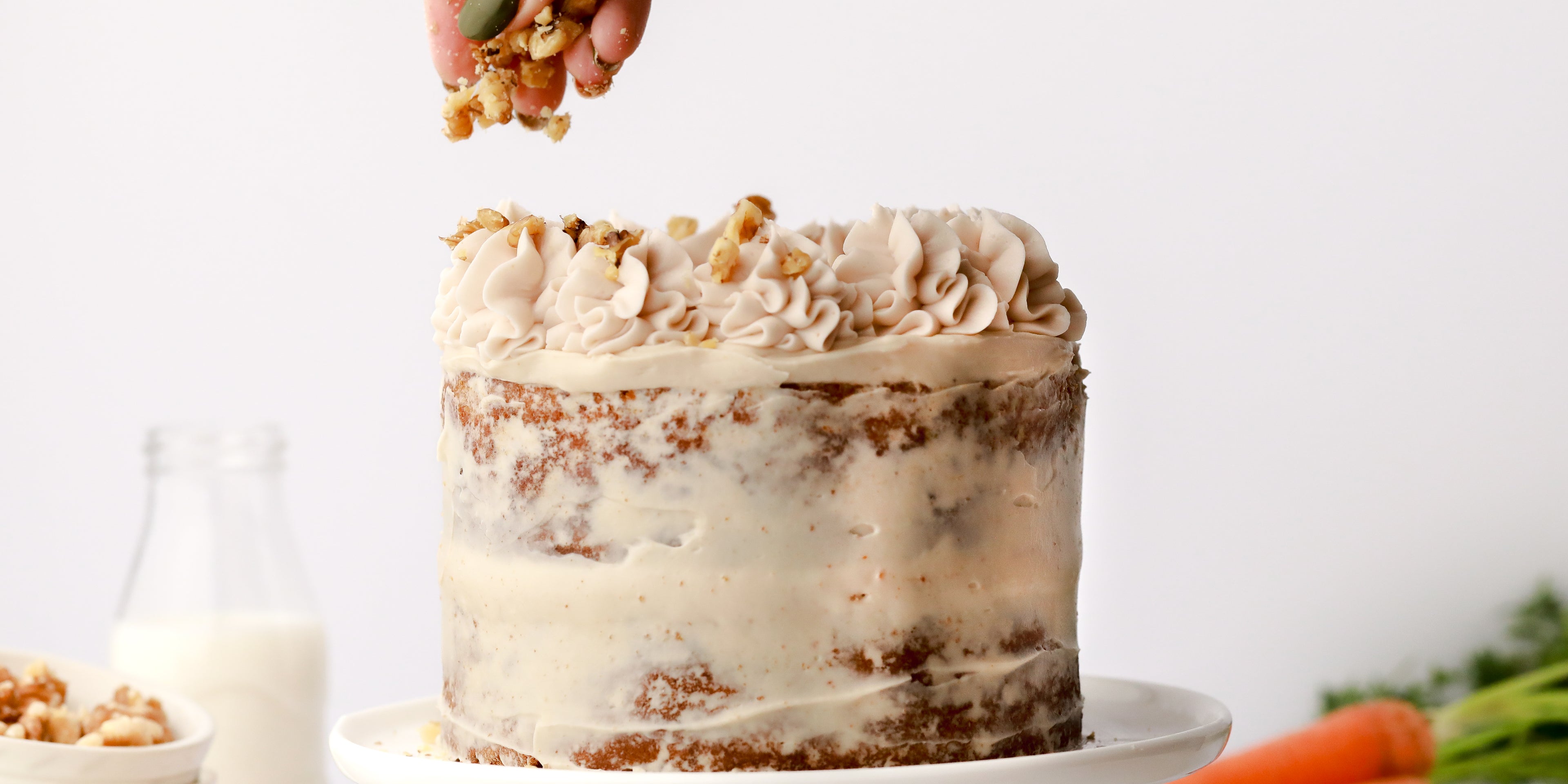 Hand sprinkling nuts on top of a carrot cake
