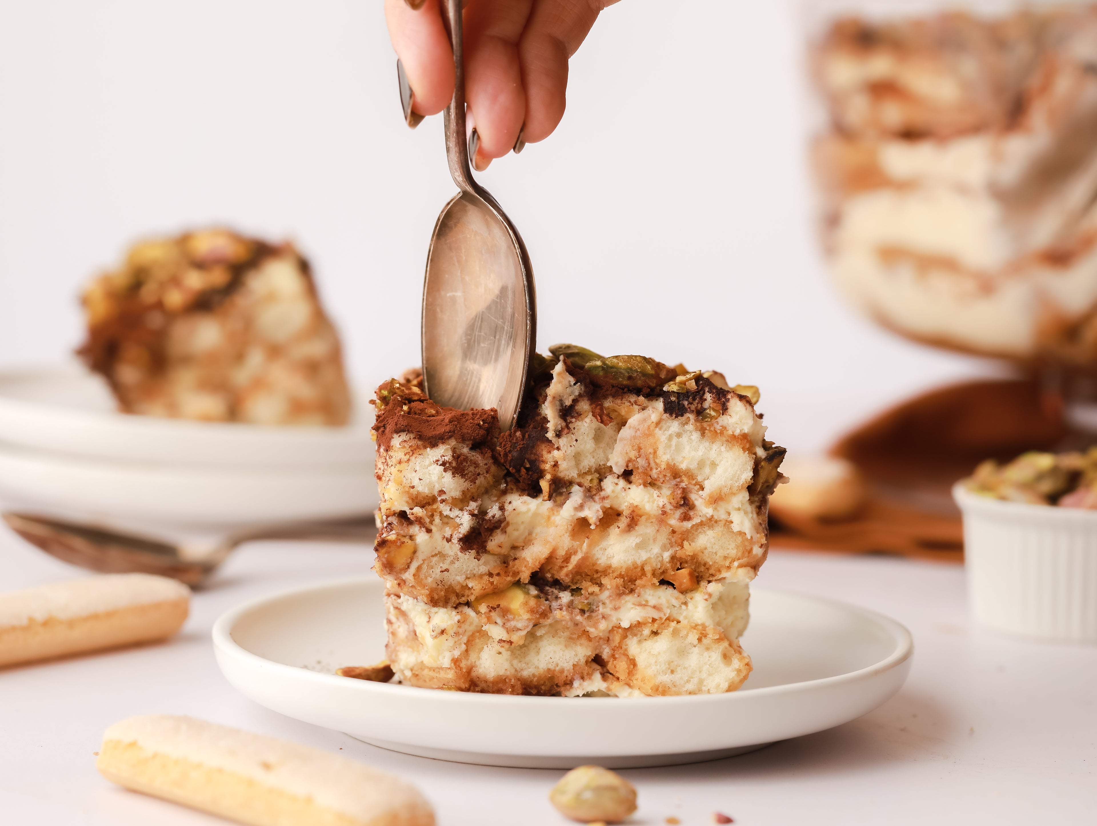 Slice of tiramisu on plate with a spoon scooping out a bite