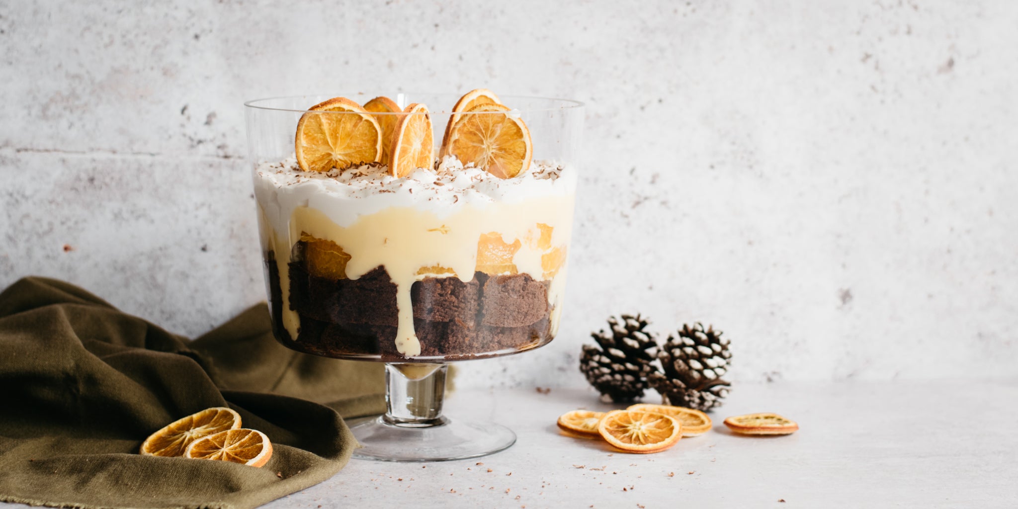 Close up of trifle dish serving Chocolate Orange Trifle with Baileys custard dripping down the sides. Next to slices of fresh orange and pine cones