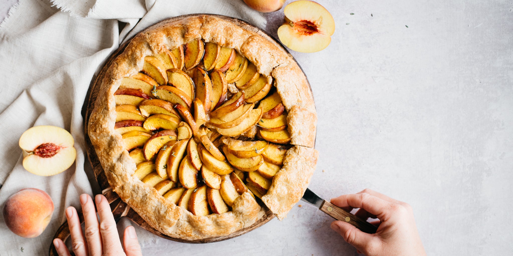 Hand removing a slice of the galette with a cake knife and peaches beside