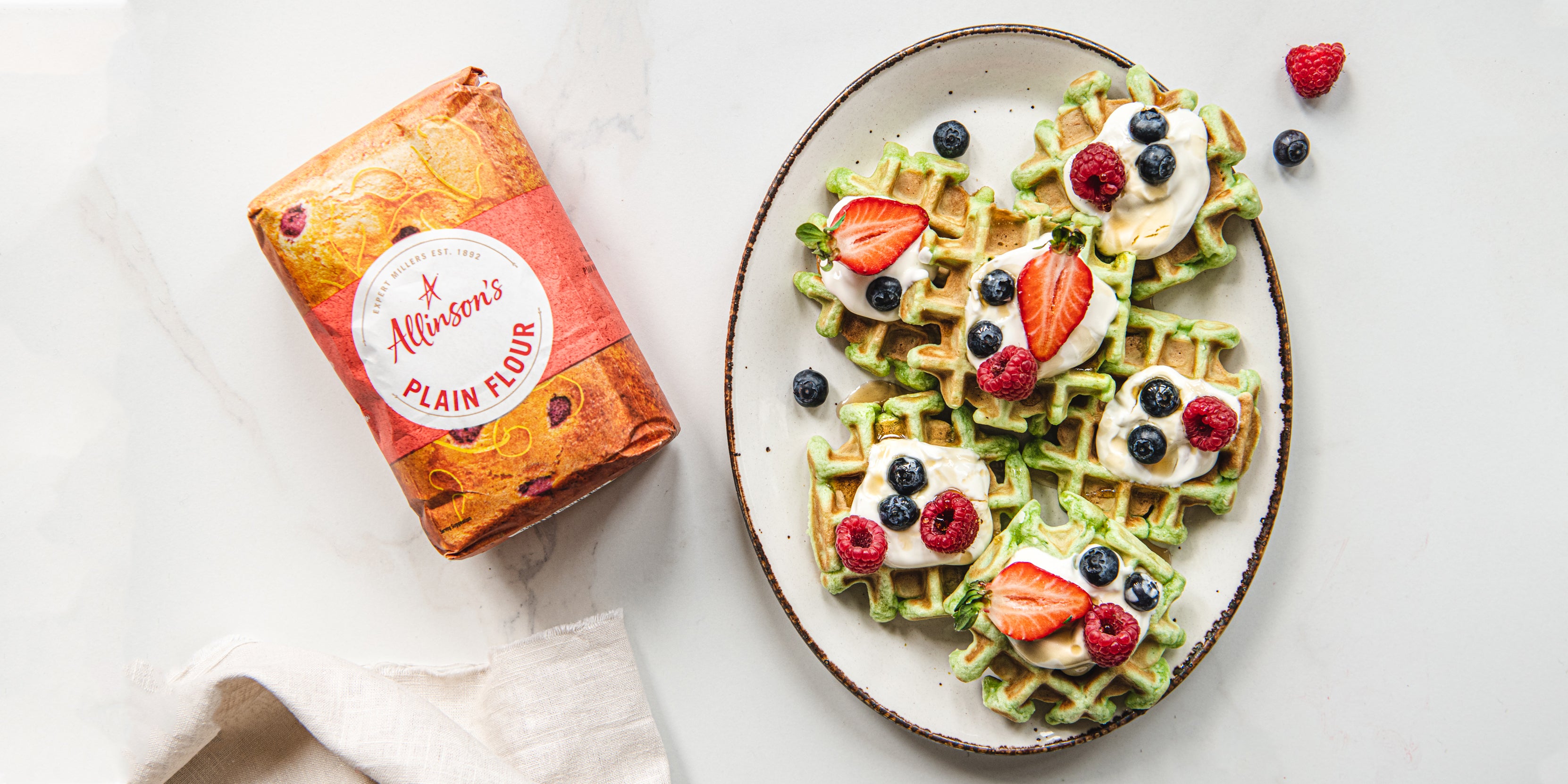 Flat lay shot of Pandan Waffles served on a plate, sprinkled with mixed berries next to a bag of Allinson's Plain flour