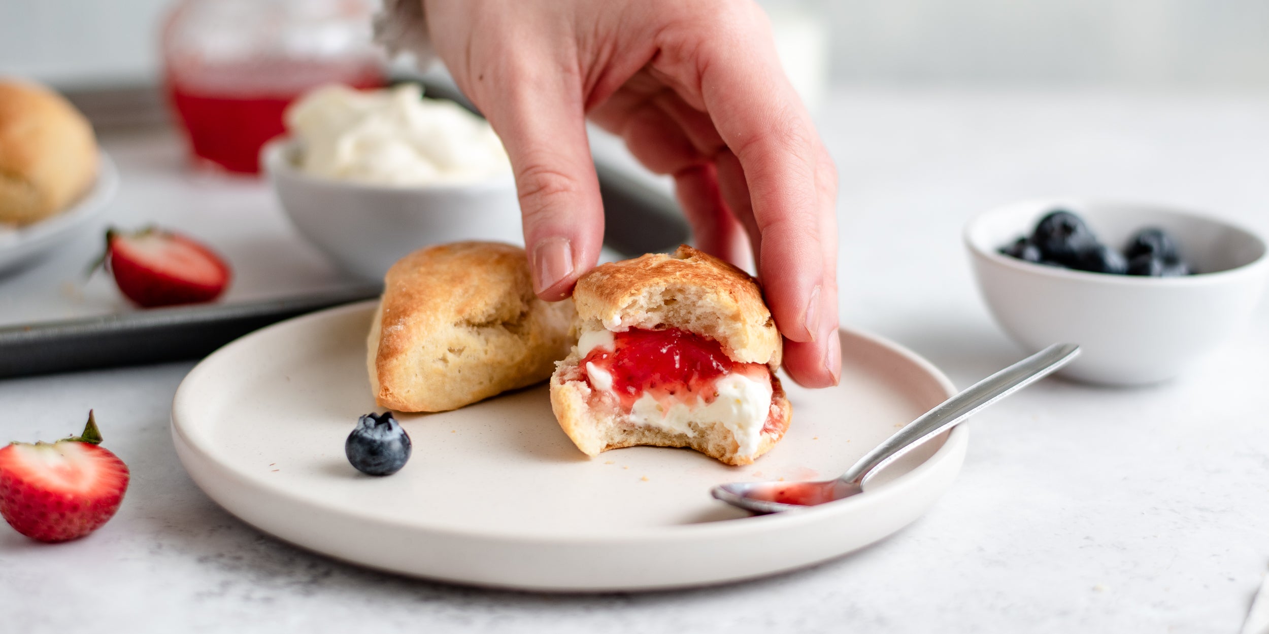 Hand reaching for an Easy Scones topped with cream and jam