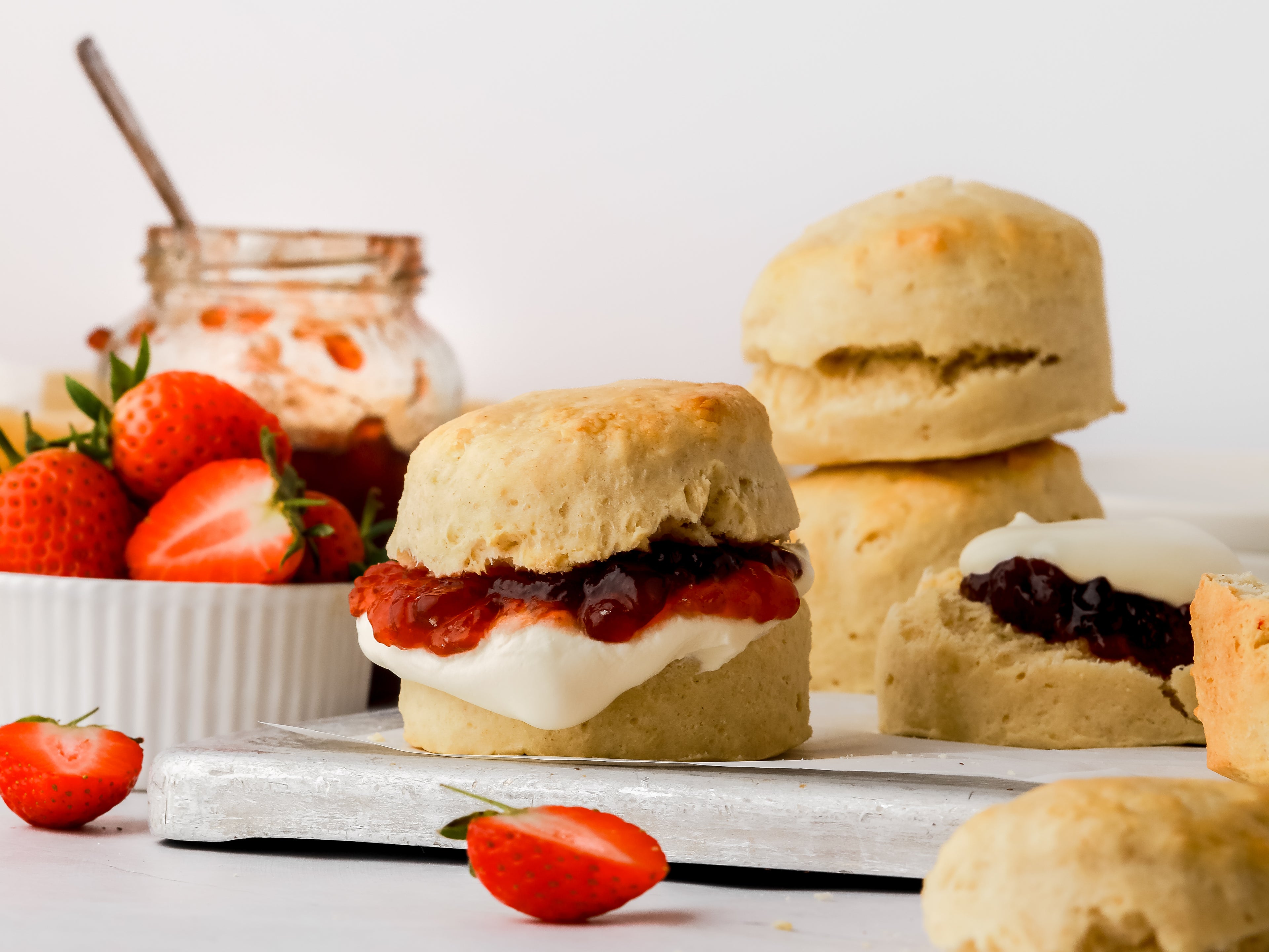 Homemade scone filled with a dollop of jam and cream with a pile of scones