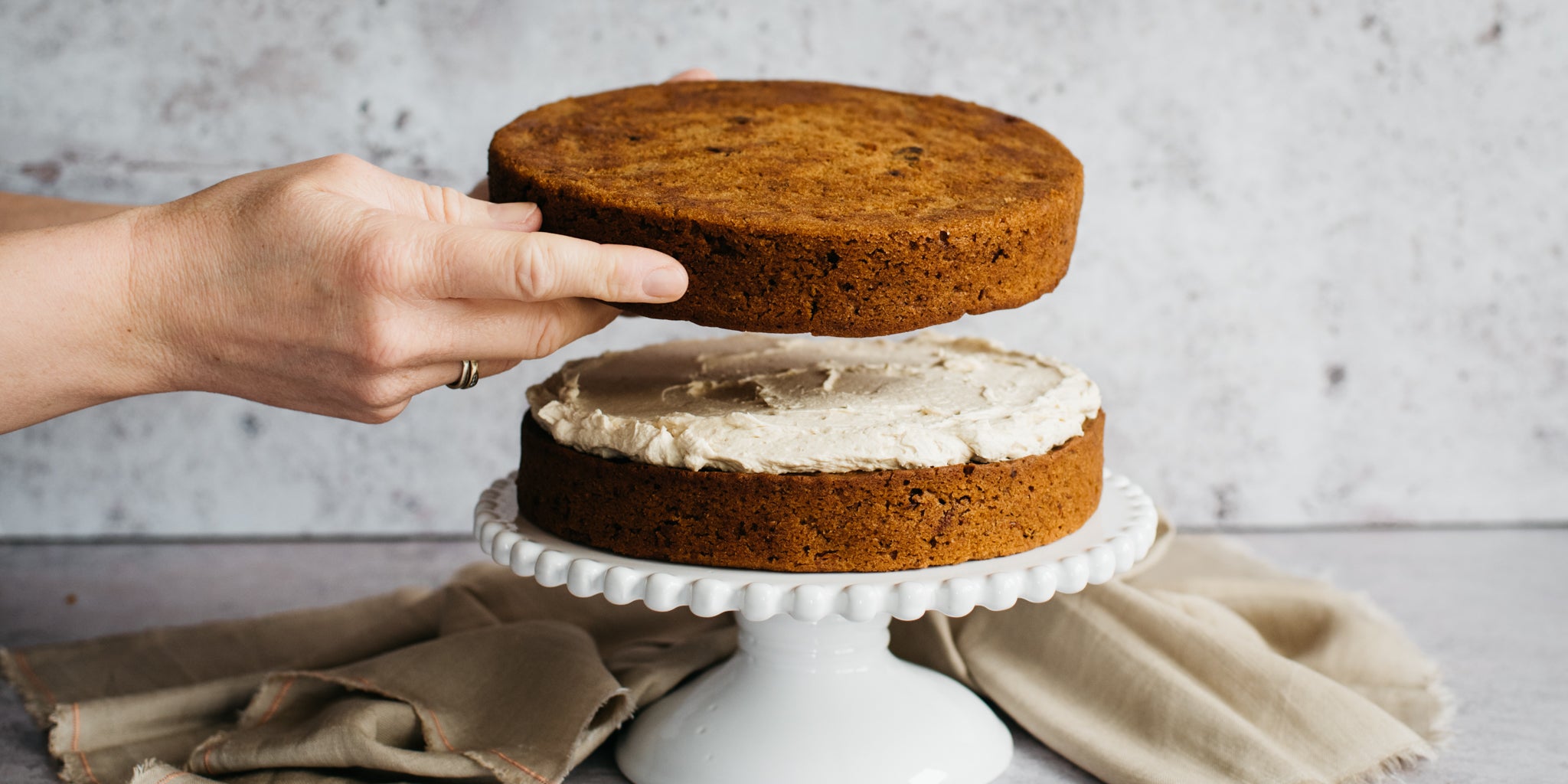 Vegan Carrot Cake being stacked with hands positioning the top Vegan Carrot Cake sponge layered ontop of Billington's Golden Icing Buttercream