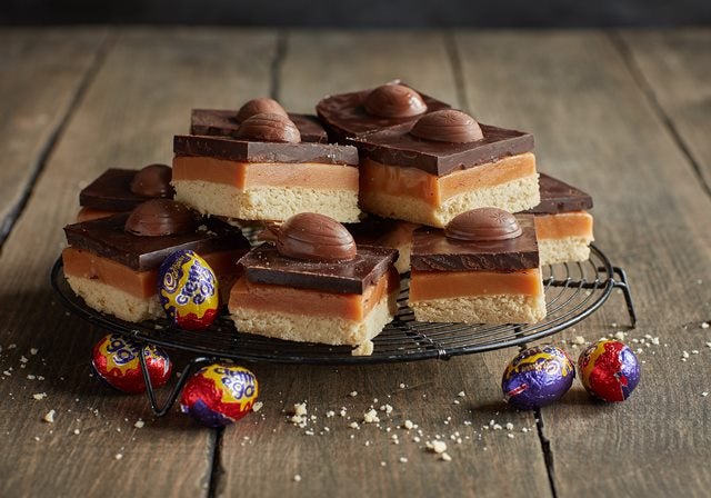 Millionaire's shortbread squares stacked up on cooling rack with creme eggs 